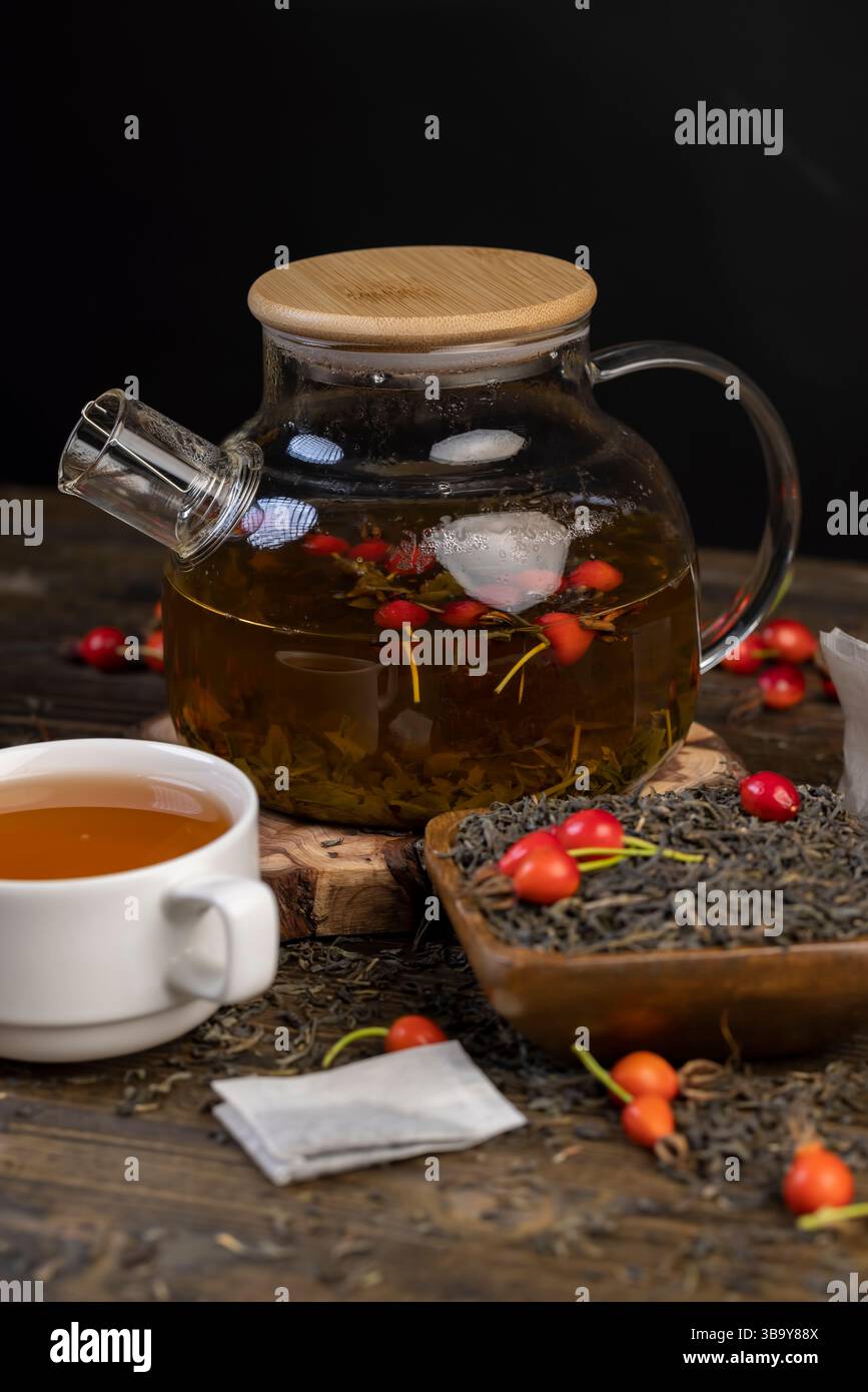 una tazza di tè caldo con frutta di rosa da vicino, frutta rosehip rossa e tè verde caldo in una teiera trasparente Foto Stock