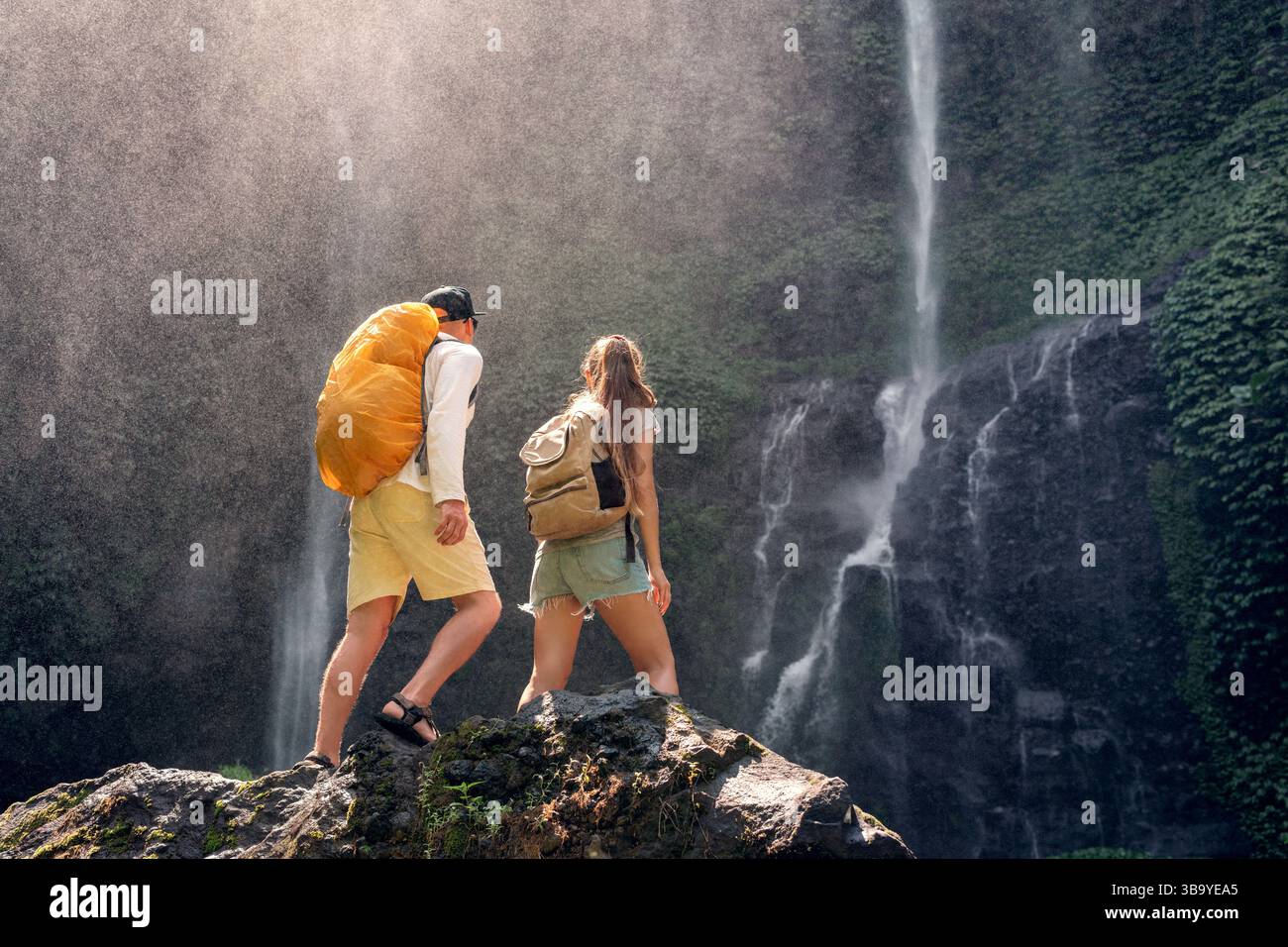 Un paio di turisti si trovano su una roccia di fronte alla cascata di Sekumpul, l'isola di Bali, Indonesia Foto Stock