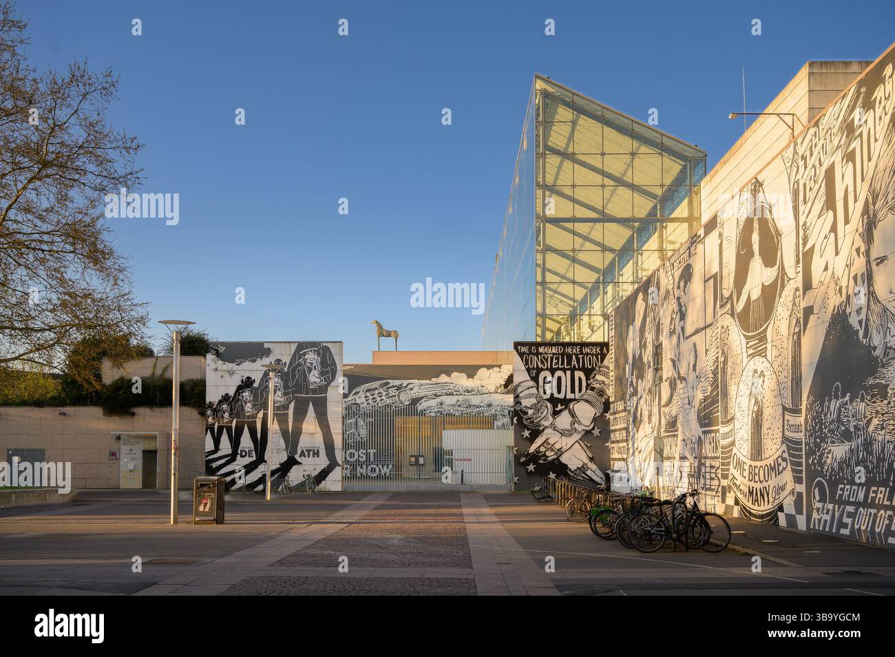 I visitatori passeggiano attraverso un vivace cortile di Strasburgo, in Francia, ammirando i grandi murales e l'arte dei graffiti che mostrano espressioni creative contro una Foto Stock