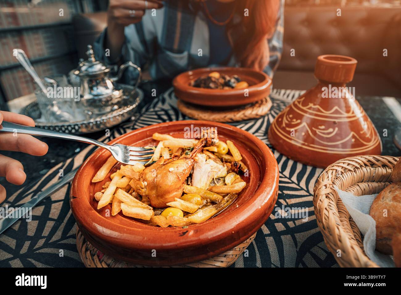 I turisti stanno consumando un tradizionale pranzo marocchino con tajine di pollo, patatine fritte e olive servite in un piatto tagine di terracotta Foto Stock
