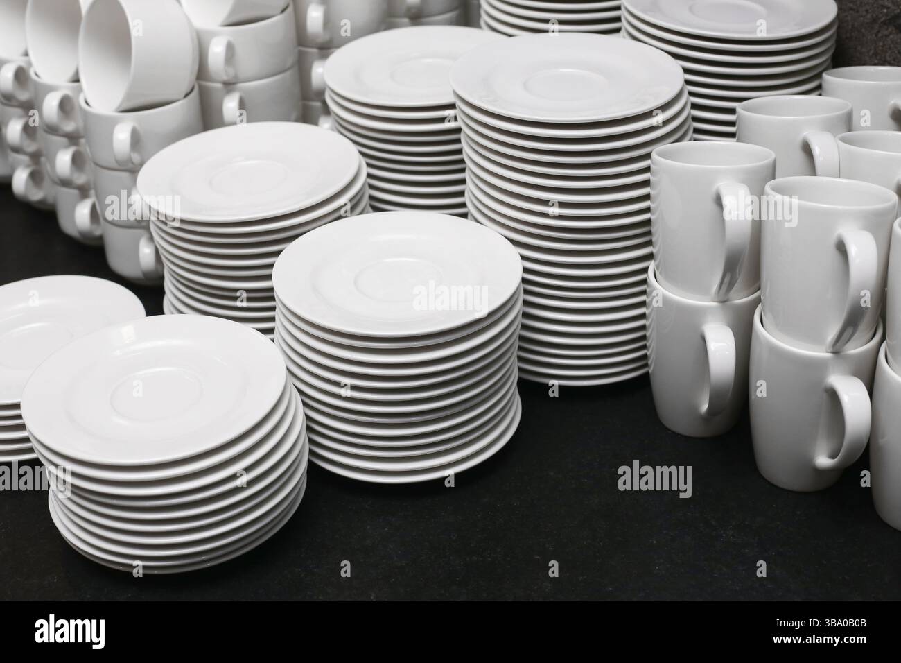 Set di stoviglie bianche impilate. Piatti, tazze e piattini. Pulire i piatti in porcellana. Attrezzature per il catering pronte. Sfondo cucina minimalista. Ristorante elegante Foto Stock