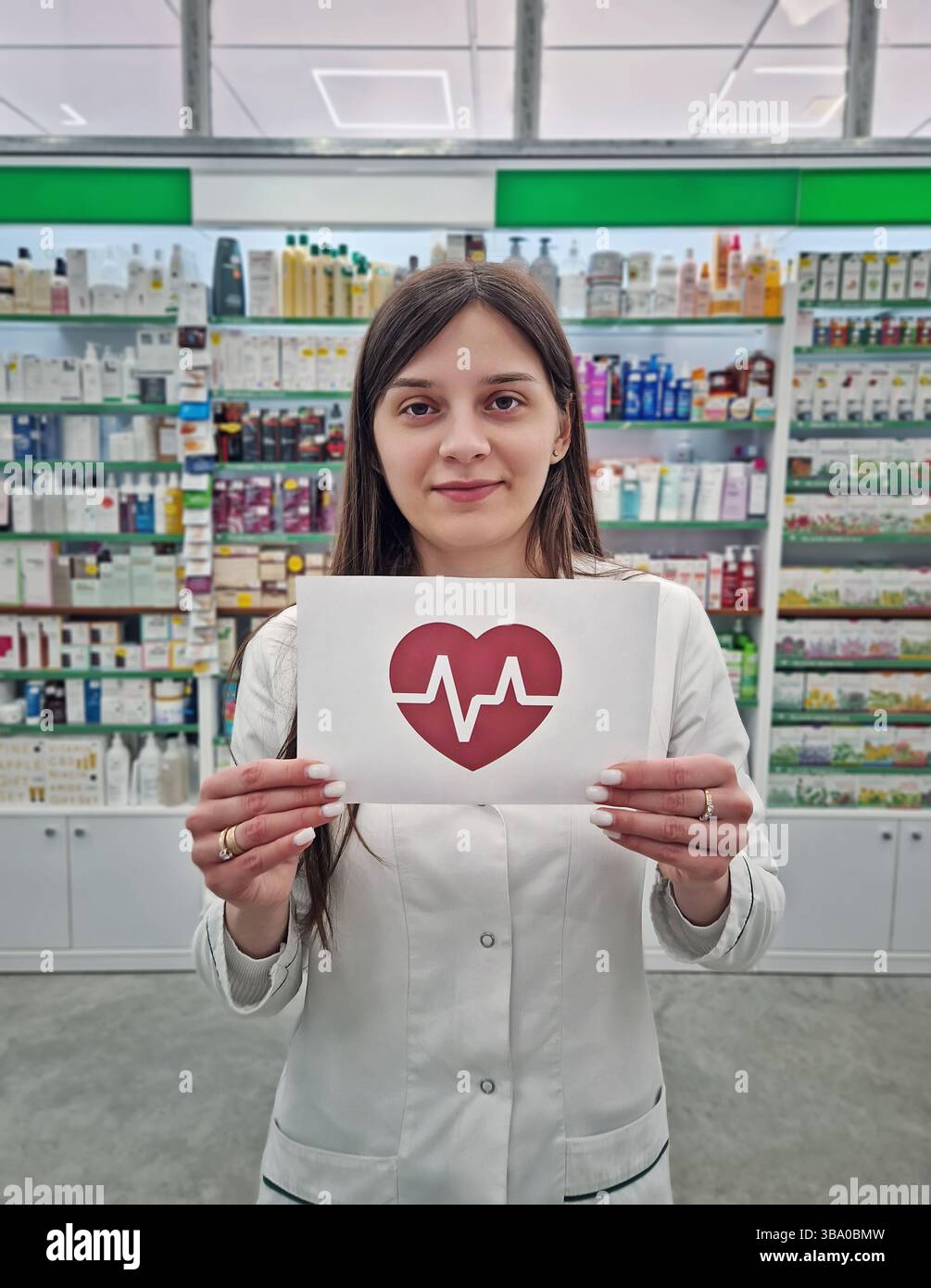 Donna lavoratrice medica o farmacista in possesso di una carta con un simbolo del cuore e un elettrocardiogramma all'interno. Concetto di salute umana e benessere. Salute - Immagine stock catturata con smartphone