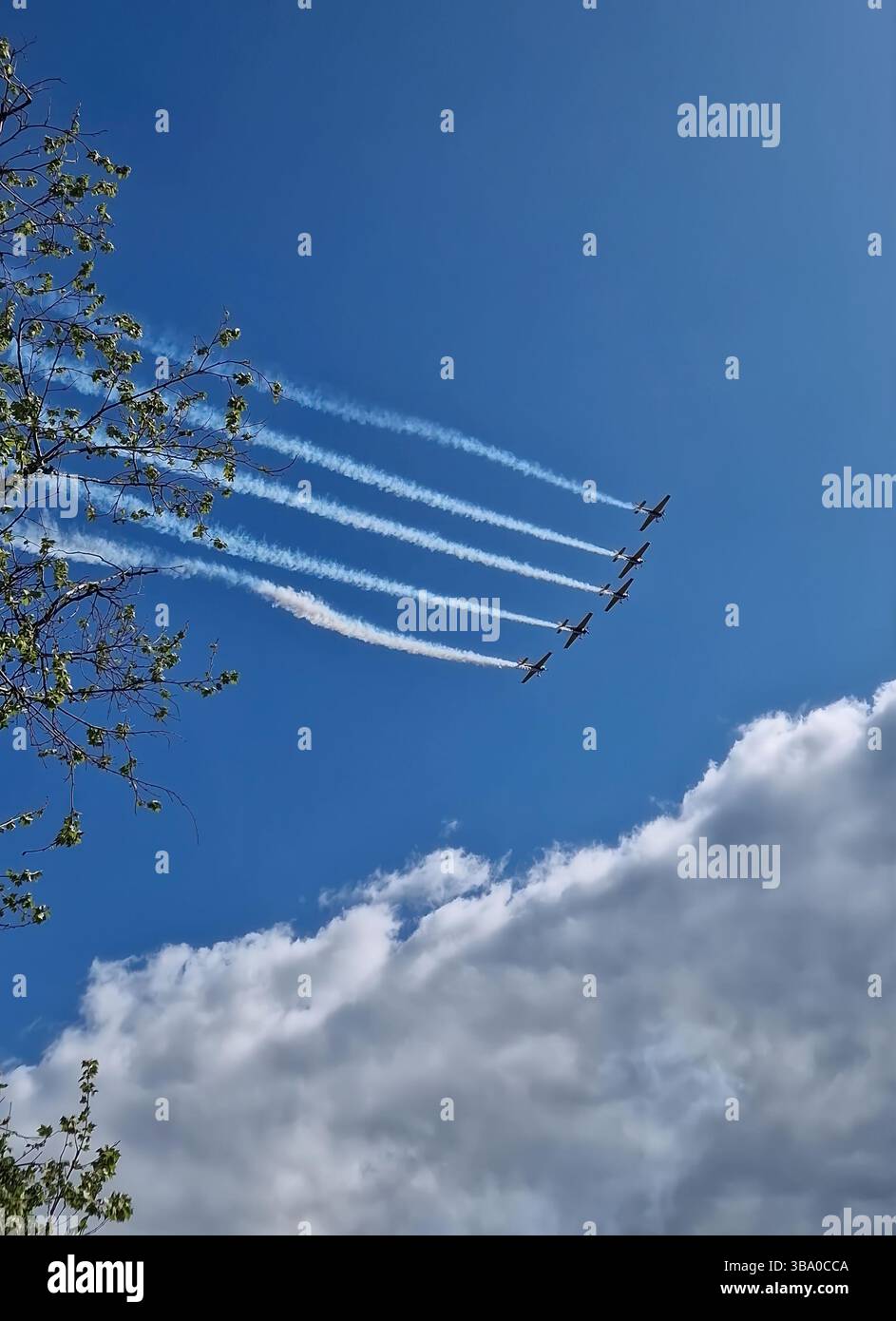 Spettacolo aereo con cinque aeroplani che volano in formazione con sentieri di fumo bianchi che si piegano verso l'alto attraverso un cielo blu luminoso disseminato di soffici nuvole Foto Stock