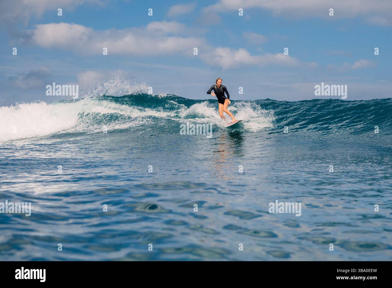 Donna surfista che cavalca un'onda blu perfetta in una giornata di sole Foto Stock