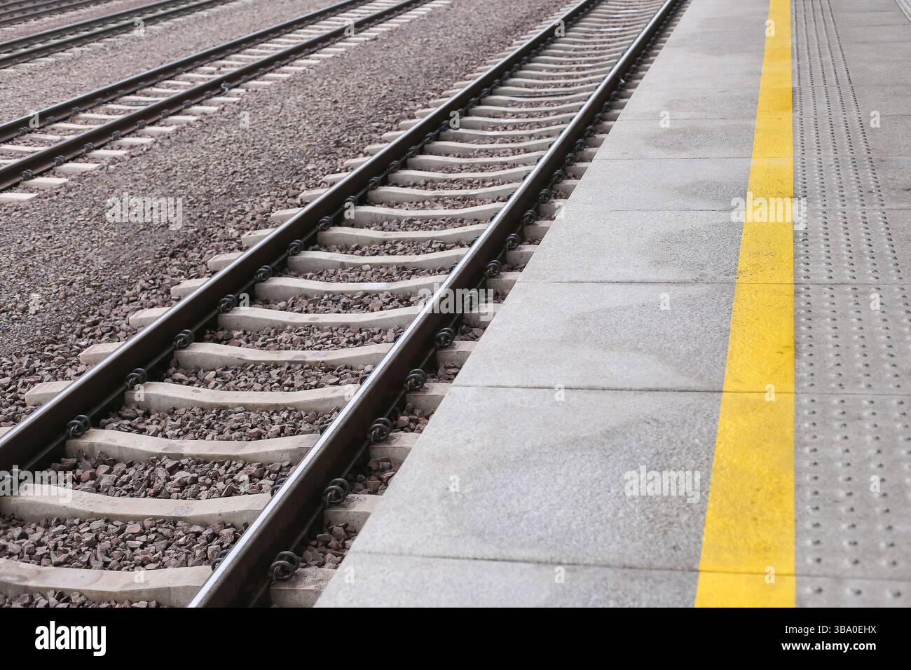 Binari ferroviari con piattaforma. Linea di sicurezza gialla visibile. Vista della stazione ferroviaria vuota. Guide in acciaio e ghiaia. Infrastrutture di trasporto urbano. Foto Stock Binari ferroviari con piattaforma. Linea di sicurezza gialla visibile. Vista della stazione ferroviaria vuota. Guide in acciaio e ghiaia. Infrastrutture di trasporto urbano. Foto Stock