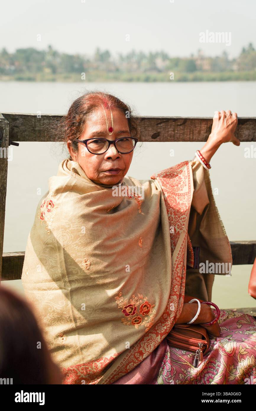 Primo piano di una donna di 73 anni con un tilak spirituale, avvolto in uno splendido scialle, seduto pacificamente su una barca sul fiume Bhagirathi in inverno. Foto Stock