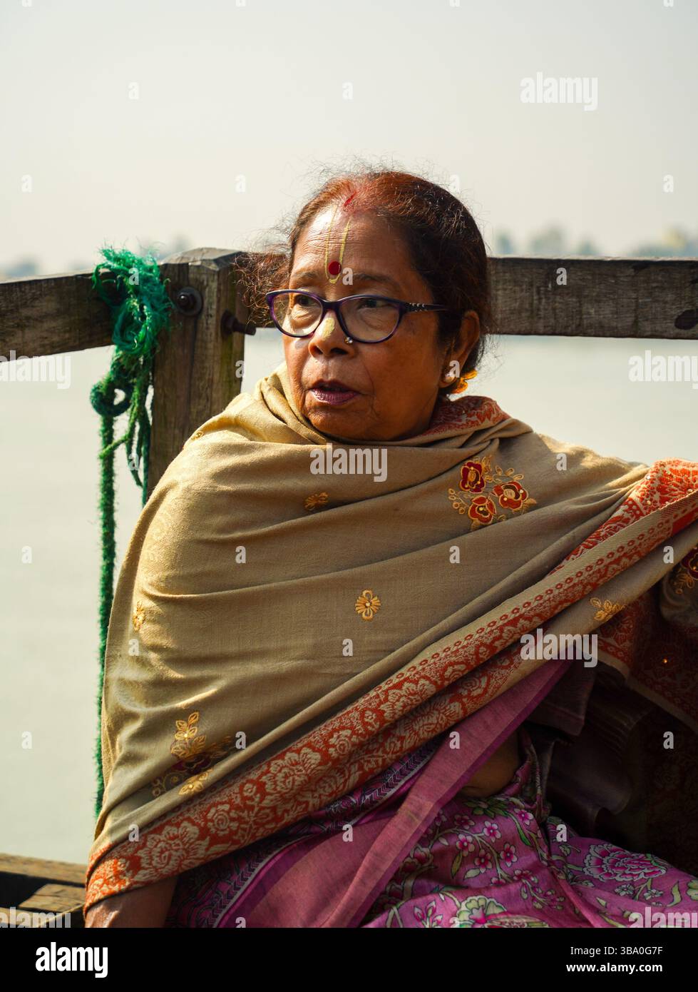Primo piano di una donna di 73 anni con un tilak spirituale, avvolto in uno splendido scialle, seduto pacificamente su una barca sul fiume Bhagirathi in inverno. Foto Stock