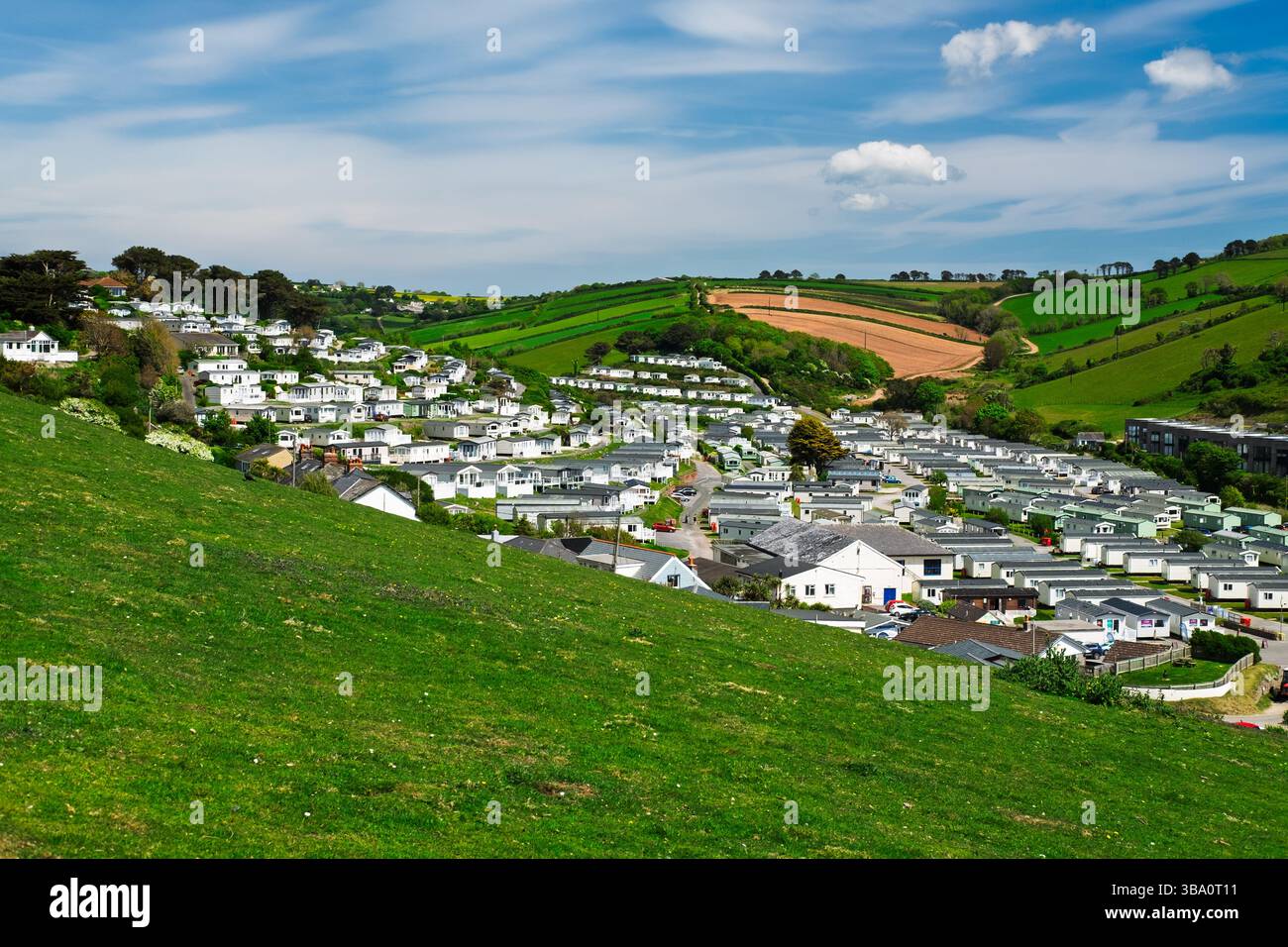 Una vista panoramica di una comunità collinare piena di case mobili annidate tra colline verdi ondulate e terreni agricoli sotto un cielo luminoso e parzialmente nuvoloso. Foto Stock