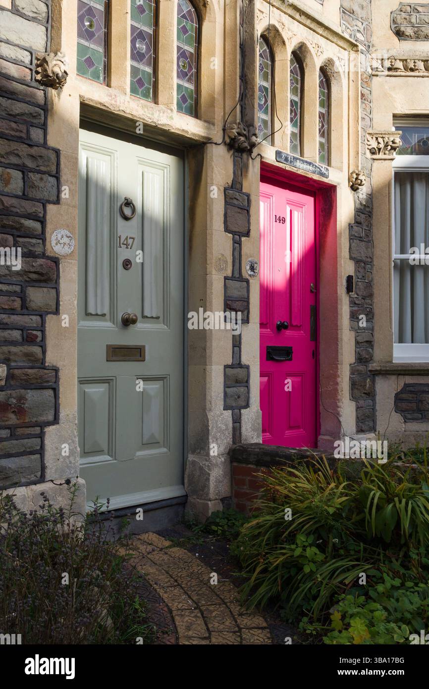 Due porte anteriori vittoriane adiacenti in una terrazza a Montpelier, Bristol, una verde, una rosa brillante, con vetrate colorate e cornici in pietra. Foto Stock