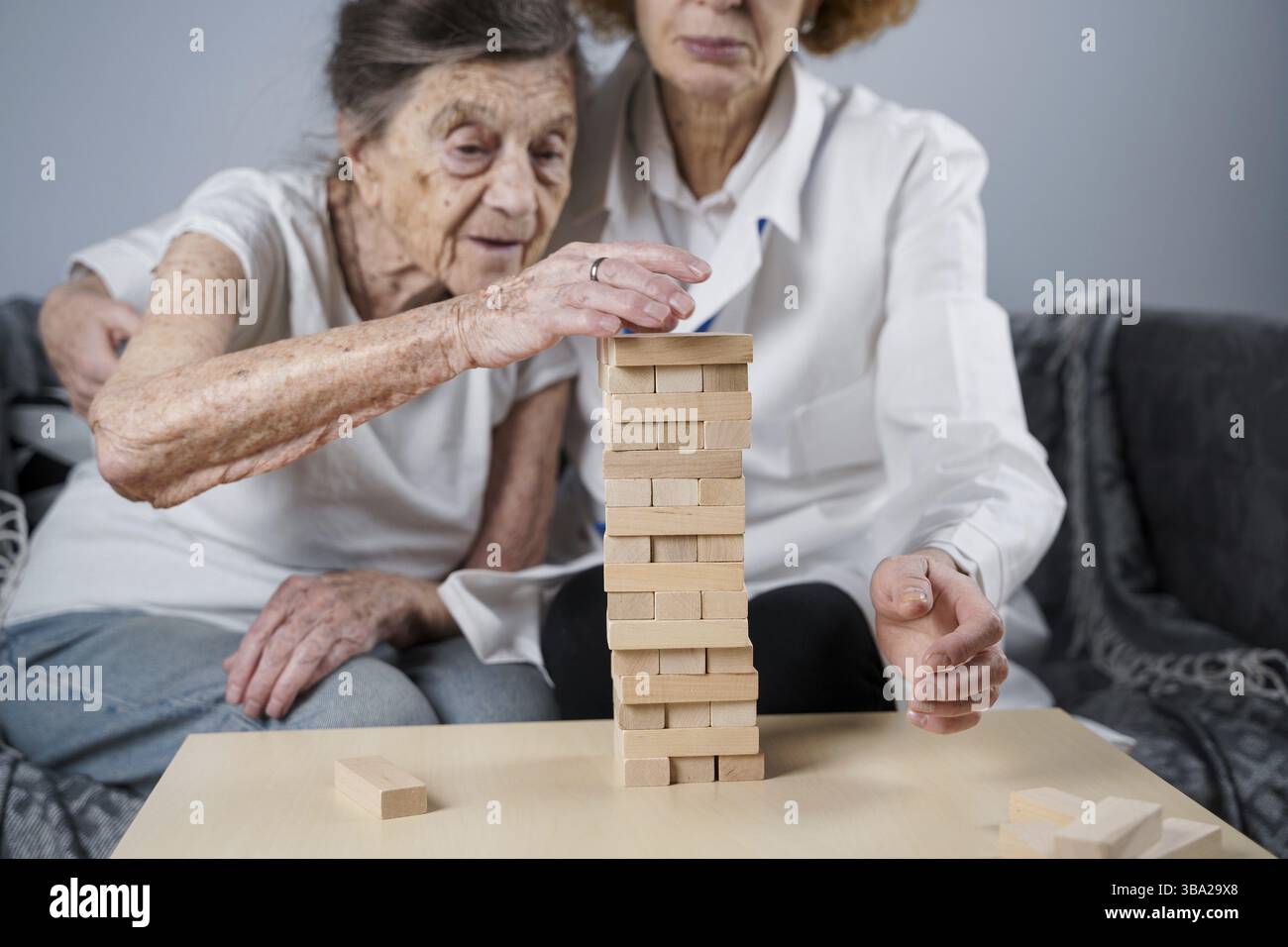 La terapia della demenza in modo giocoso, addestrando le dita e le abilità motorie fini, costruisce i blocchi di legno nella torre, giocando Jenga. Donna anziana di 90 anni e. Foto Stock
