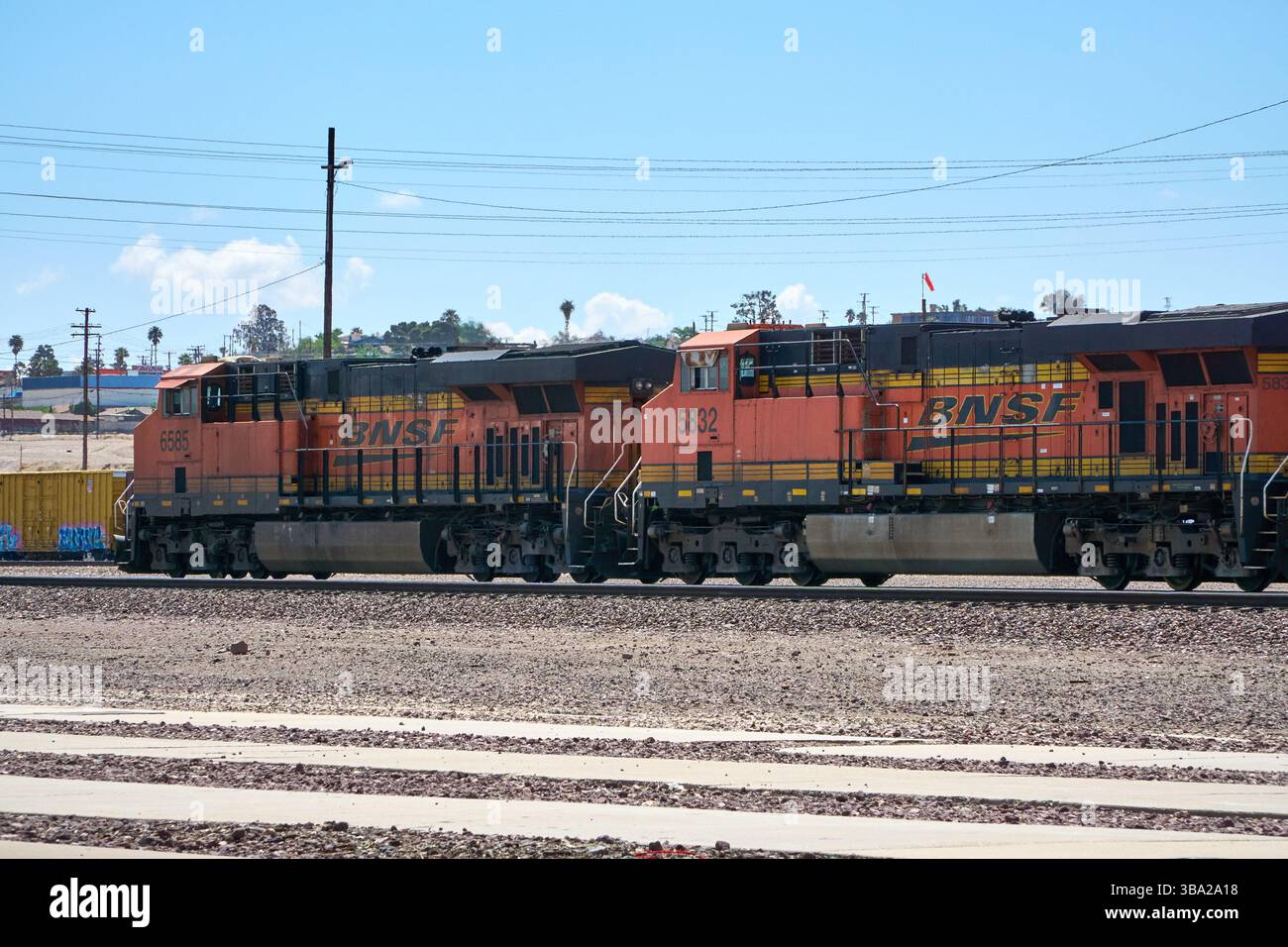 7 maggio 2025, Barstow, California, Stati Uniti: Fotografata nel cantiere ferroviario di Barstow, questa linea di locomotive della BNSF Railway si trova al di sotto di un cavalcavia del deserto, arancione brillante e nero contro le sfumature del Mojave. Questi cavalli da lavoro General Electric fanno parte del ritmo quotidiano di uno dei corridoi merci più trafficati negli Stati uniti occidentali.attaccati a una lunga serie di tramogge coperte, che probabilmente trasportano grano o materiali secchi sfusi, le locomotive riflettono la portata e l'efficienza della moderna logistica ferroviaria. Barstow funge da nodo critico nel sistema BNSF, dove i treni sono ri-cr Foto Stock