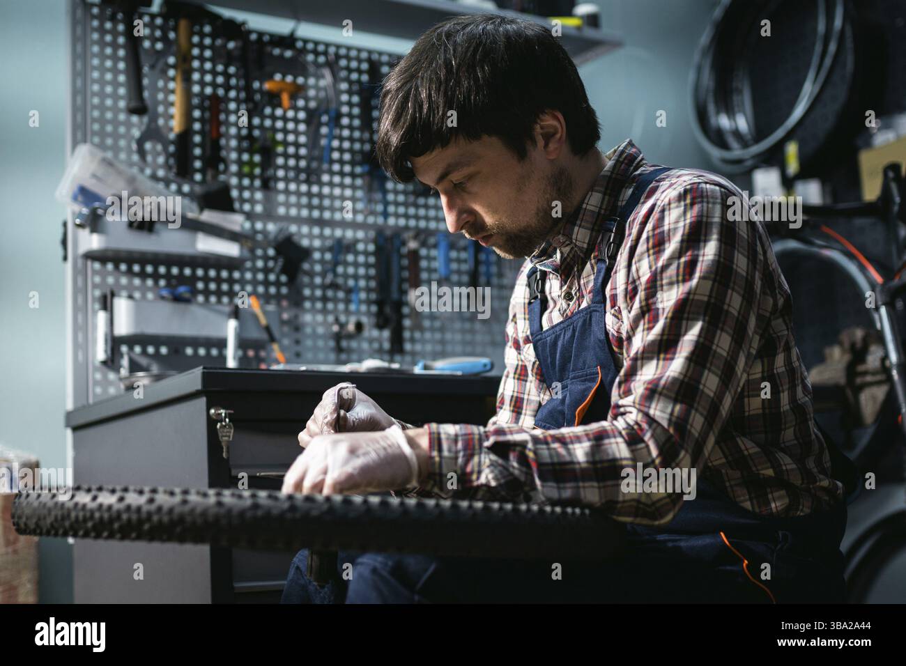 Giovane riparatore caucasico che ripara la ruota di mountain bike in officina di bike shop. Fissaggio bicicletta. Cura per voi ruote. Uomo meccanico che lavora in garage. Foto Stock