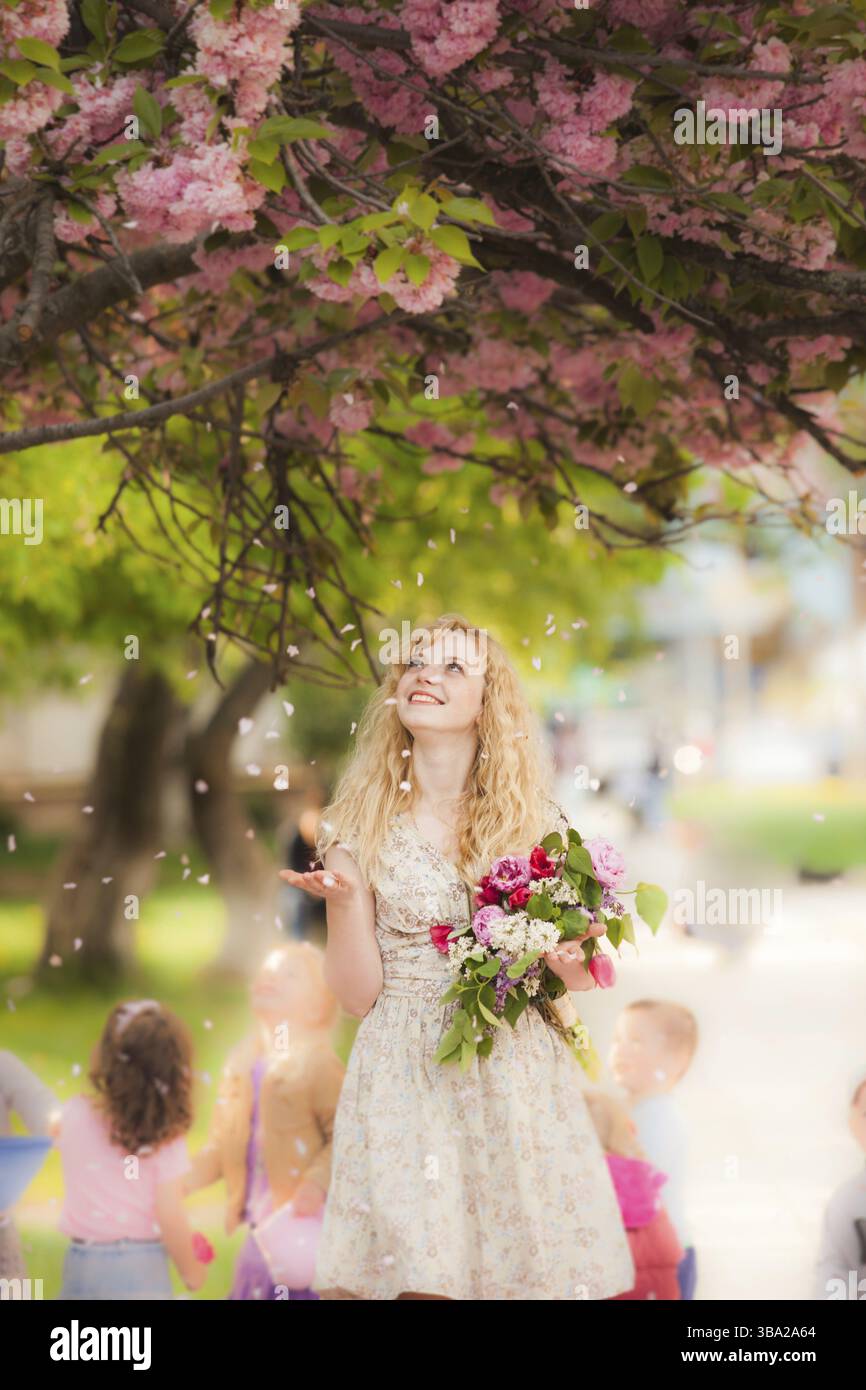 La ragazza sotto l'albero sakura con i fiori nelle mani gode la fioritura Foto Stock