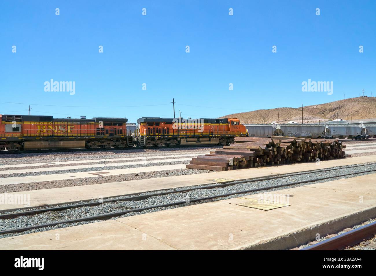 7 maggio 2025, Barstow, California, Stati Uniti: Fotografata nel cantiere ferroviario di Barstow, questa linea di locomotive della BNSF Railway si trova al di sotto di un cavalcavia del deserto, arancione brillante e nero contro le sfumature del Mojave. Questi cavalli da lavoro General Electric fanno parte del ritmo quotidiano di uno dei corridoi merci più trafficati negli Stati uniti occidentali.attaccati a una lunga serie di tramogge coperte, che probabilmente trasportano grano o materiali secchi sfusi, le locomotive riflettono la portata e l'efficienza della moderna logistica ferroviaria. Barstow funge da nodo critico nel sistema BNSF, dove i treni sono ri-cr Foto Stock