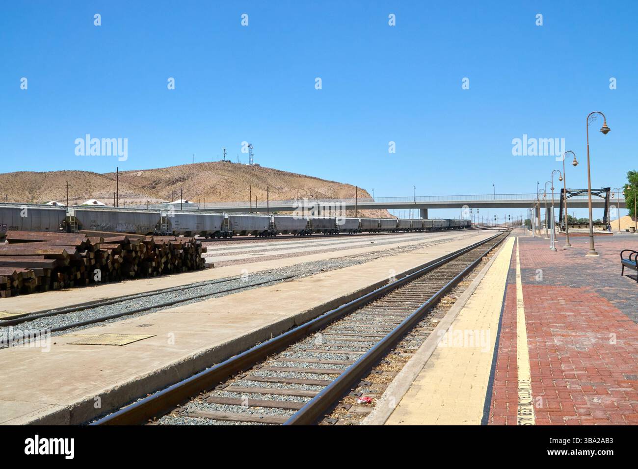 Barstow, California, Stati Uniti. 7 maggio 2025. Fotografata dal bordo della piattaforma Amtrak di Barstow, questa scena cattura l'ampia estensione di uno dei più grandi e trafficati cantieri ferroviari degli Stati uniti occidentali. Una serie di tramogge coperte si estende in lontananza sotto un cielo desertico, mentre pile di ferrovie inutilizzate attendono silenziosamente accanto ai binari.questa vista''”vuota di persone ma densa di infrastrutture''”rivela la portata e l'intensità silenziosa del ruolo di Barstow nel movimento merci americano. La piattaforma in mattoni rossi contrasta con le viuzze pallide e polverose di acciaio e cemento che si estendono Foto Stock