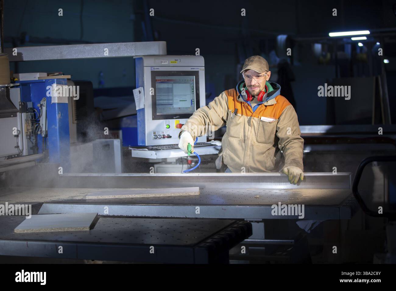 Un lavoratore di produzione di mobili dietro una macchina programmata produce parti di mobili. Produzione di mobili Foto Stock
