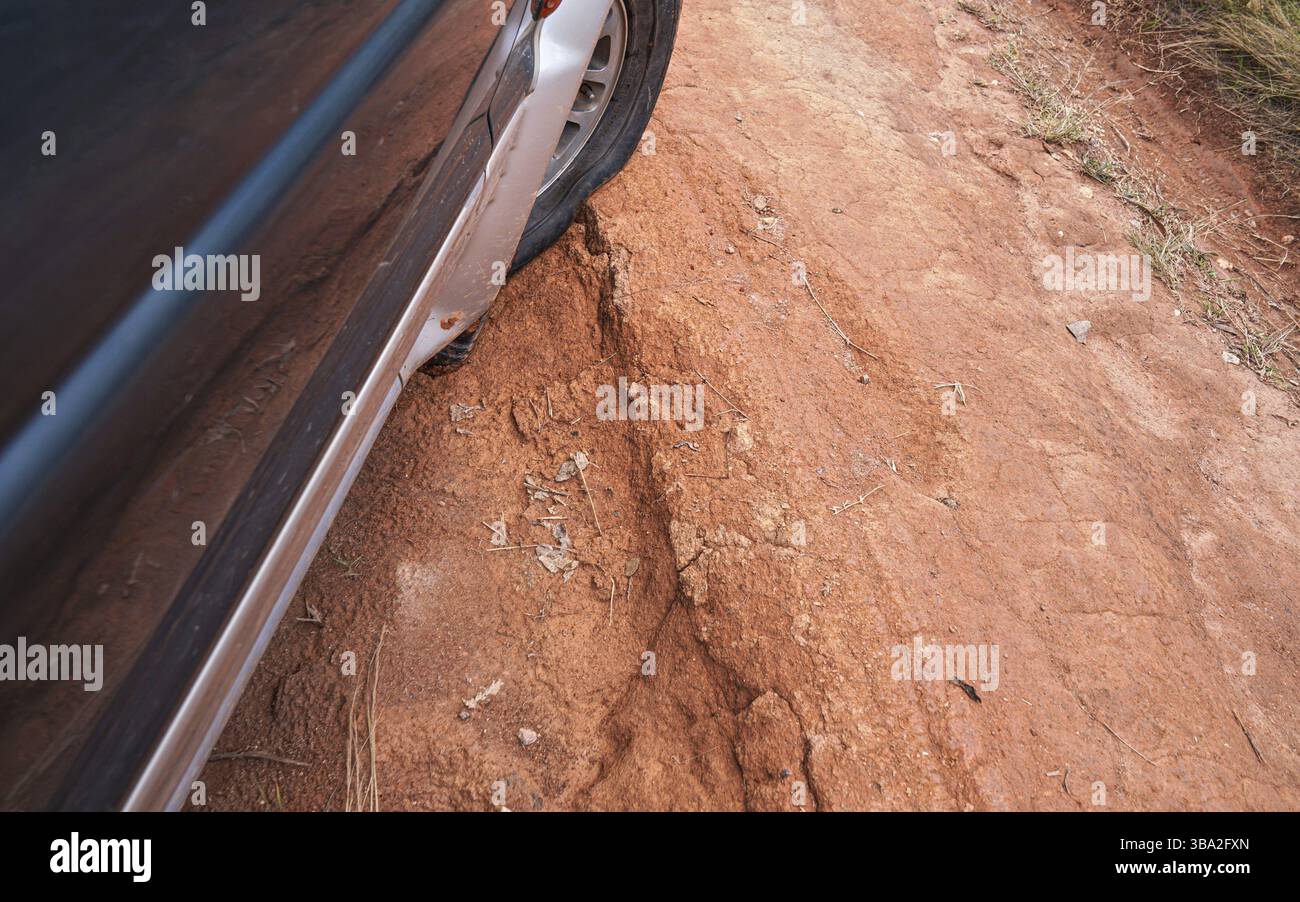 Guida di un veicolo a trazione integrale su una strada di campagna polverosa rossa con grandi fori, dettaglio su pneumatici con bassa pressione su terreni accidentati. Le strade sono in cattive condizioni Foto Stock