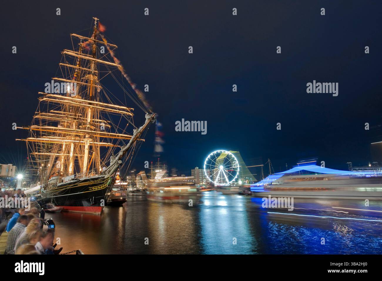 Naviga ad Amsterdam, sul canale IJ, sulla nave a vela illuminata e sugli spettatori, sulla ruota panoramica e sui sentieri leggeri delle barche di passaggio. Copia spazio. Foto Stock