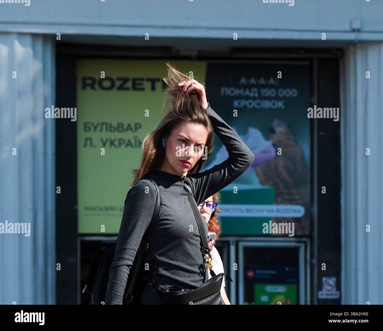 Kiev, Ucraina - 1° maggio 2025: Ritratto di una giovane donna elegante che si adatta i capelli mentre cammina di fronte a un negozio Rozetka a Kiev, Ucraina, che mostra uno scorcio della vita quotidiana nella vivace città Foto Stock