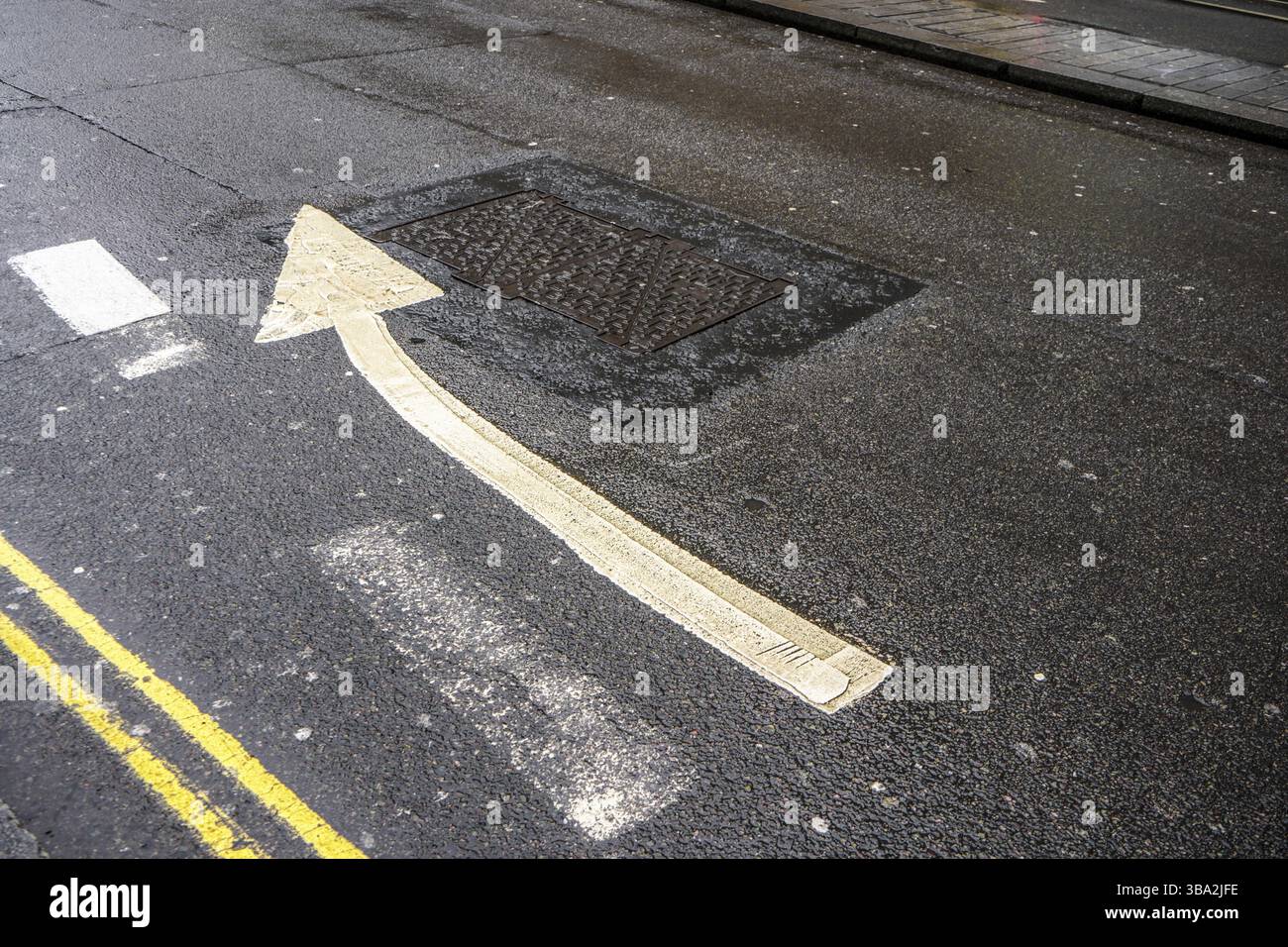 Doppia linea gialla e freccia che puntano leggermente a destra su asfalto umido, Londra, Regno Unito, Europa Foto Stock