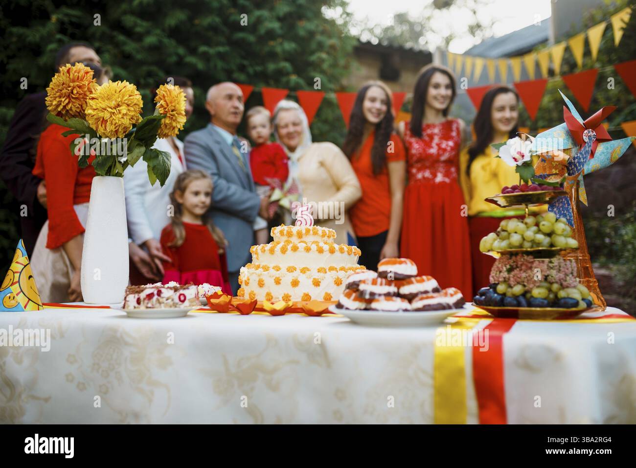 Festa di famiglia, compleanno, bimbo fuori nel cortile. Grande festa in giardino. Focalizzazione selettiva sulla torta con una candela di 5 anni, gente sfocata grande f Foto Stock