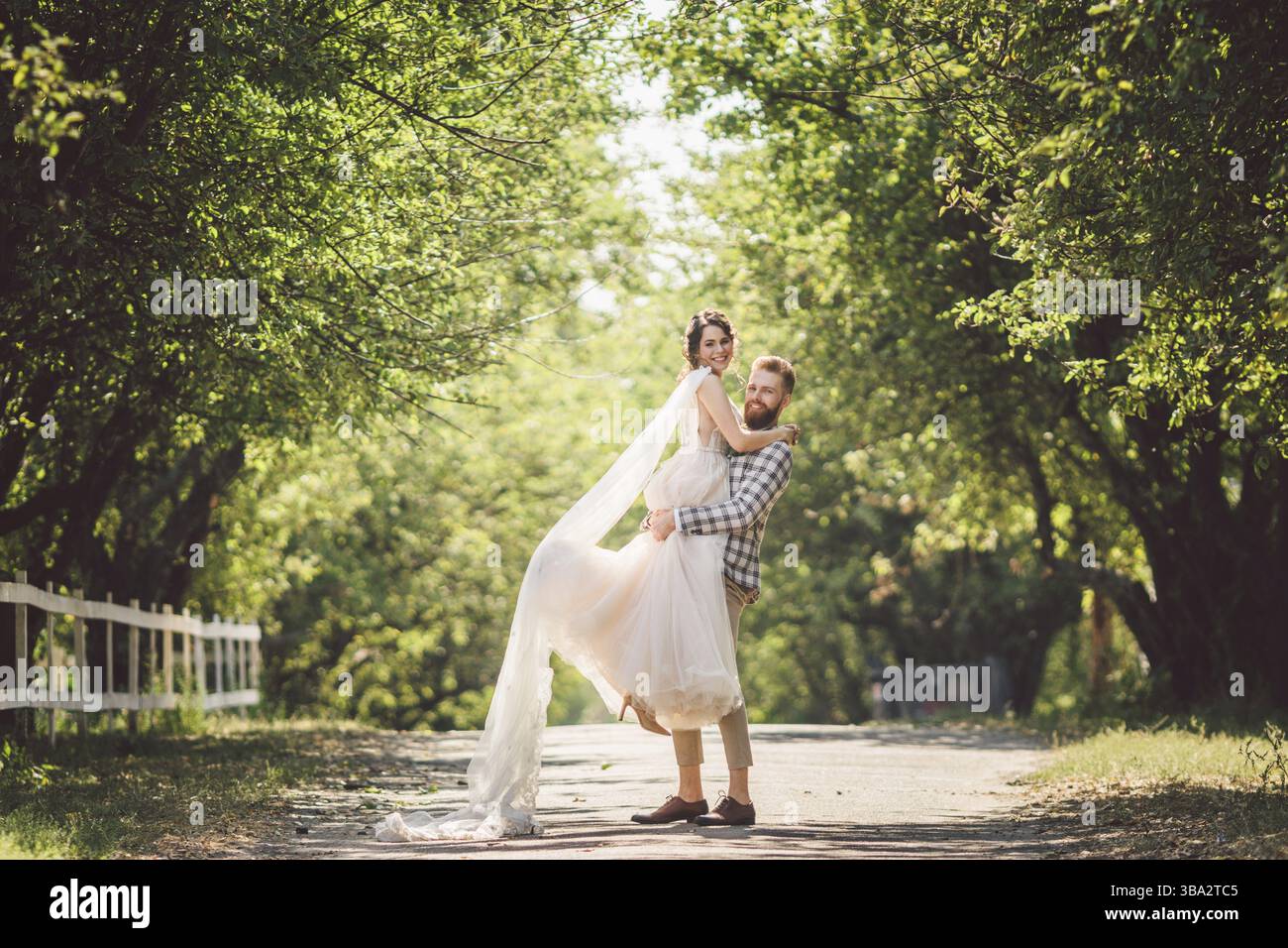 Lo sposo felice solleva la sposa nel parco estivo. l'uomo ha cresciuto e abbracciato la donna alle sue braccia. Coppia sposata di recente nel parco. Solo sposato. Cammina nel parco An Foto Stock