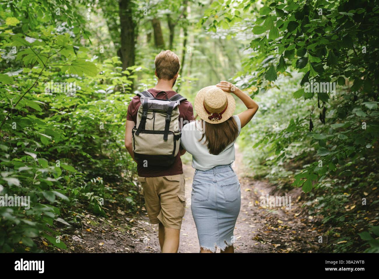 Coppia che si tiene per mano camminando nella foresta, vista posteriore. Avventura, viaggi, turismo, escursioni, gente. Vista posteriore di due persone che trasportano lo zaino mentre camminano Foto Stock
