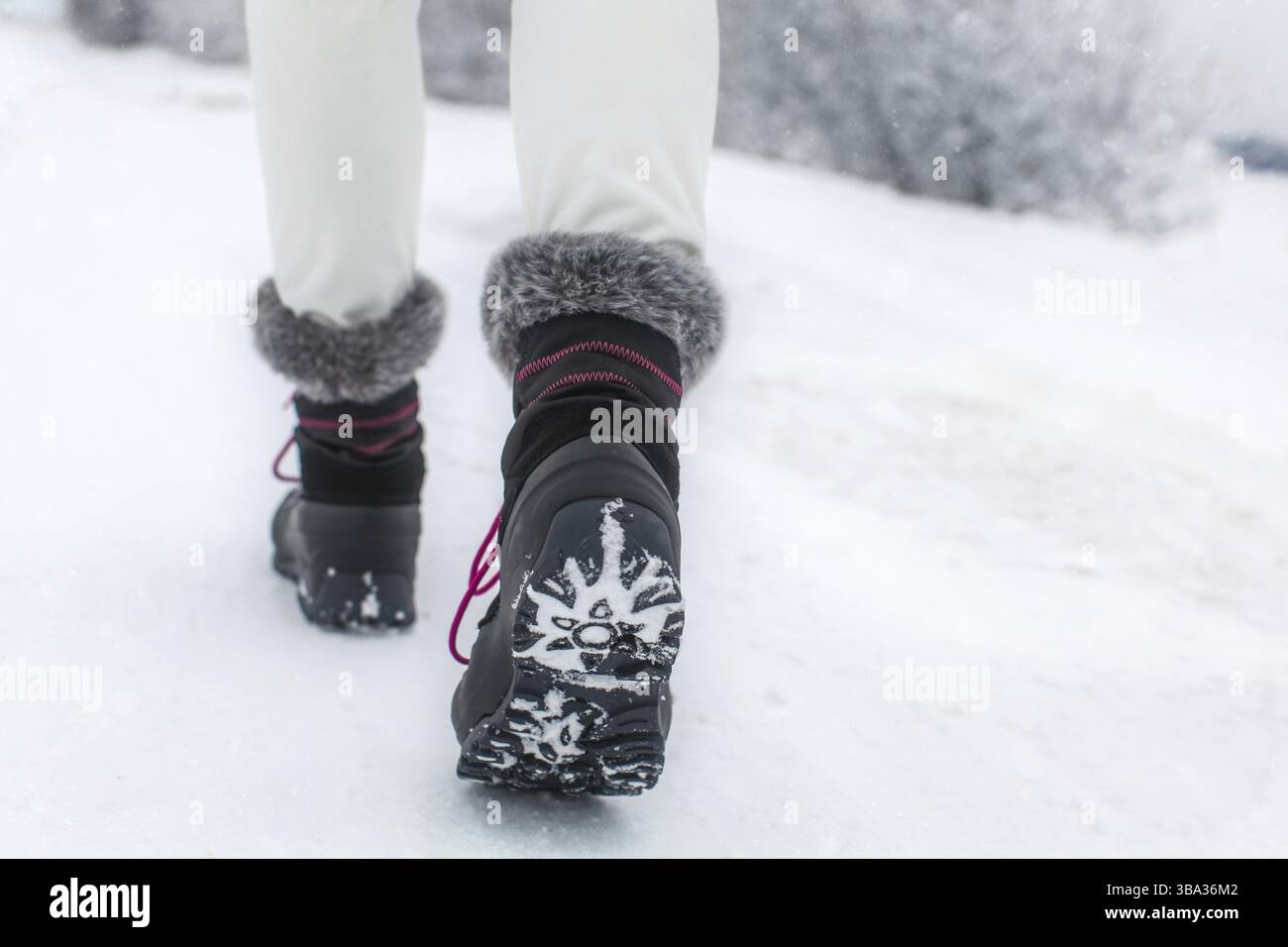 Dettaglio della donna che solleva lo stivale nero e grigio con pelliccia sintetica e lacci viola, mostrando il battistrada degli stivali, girato in un giorno coperto d'inverno Foto Stock