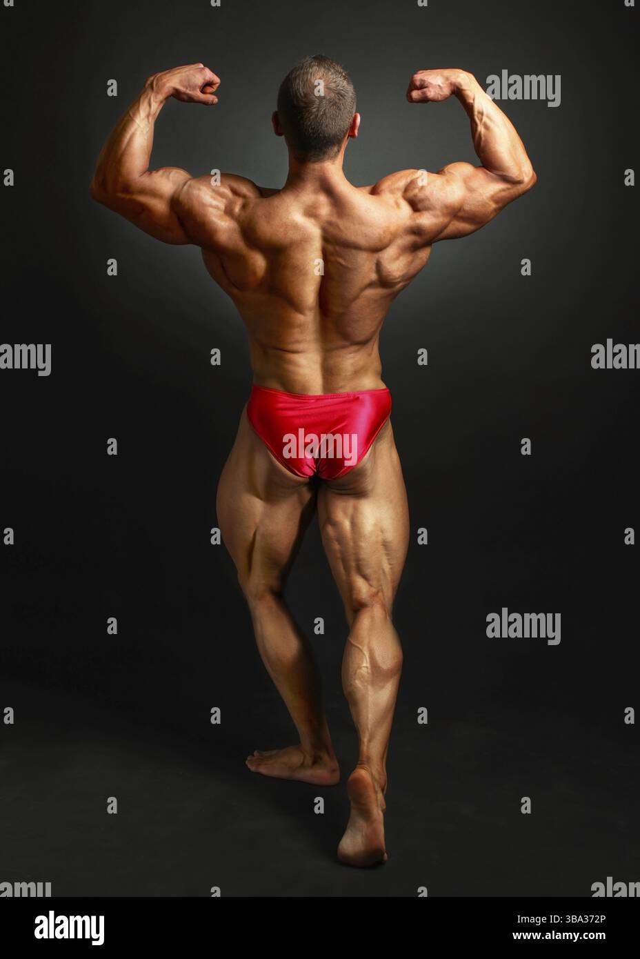 Giovane uomo bodybuilder flessione back Doppio bicpes pongono, mostrando il suo enorme trapezius, romboidale, levator, latissimus dorsi e i muscoli delle gambe. Studio shot o Foto Stock