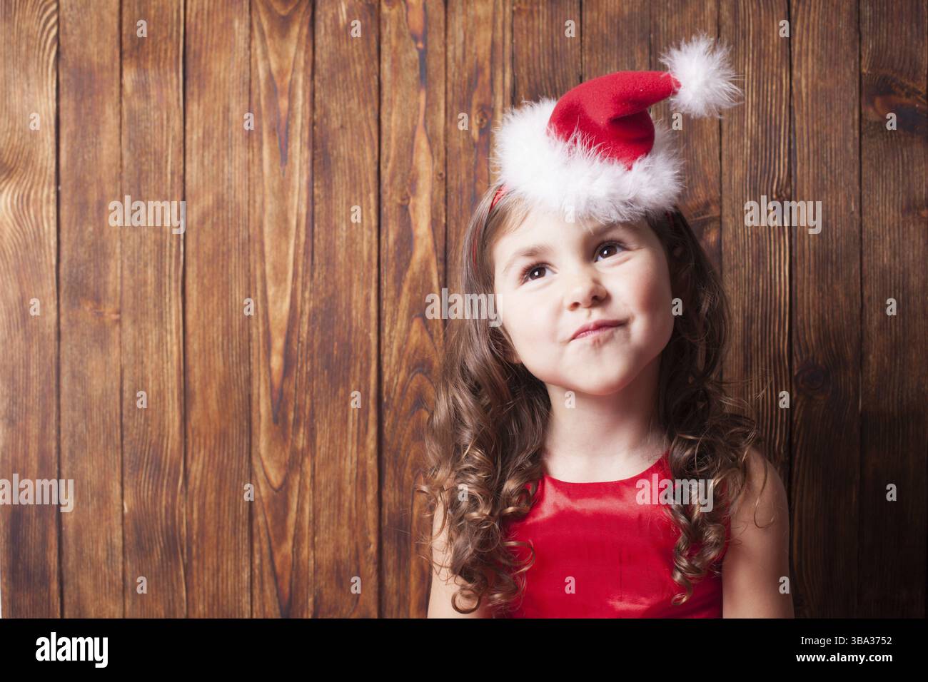 Ragazza in Babbo Natale fascia seduta su parete di legno, spazio copia Foto Stock