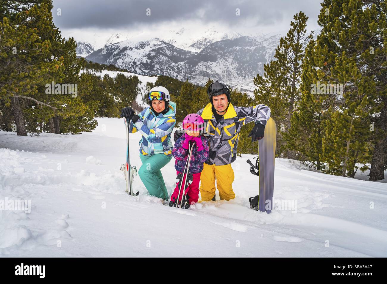 Famiglia, madre, padre e figlia in piedi nella neve profonda e tenendo sci e snowboard. Vacanze invernali ad Andorra, El Tarter, Pirenei Foto Stock