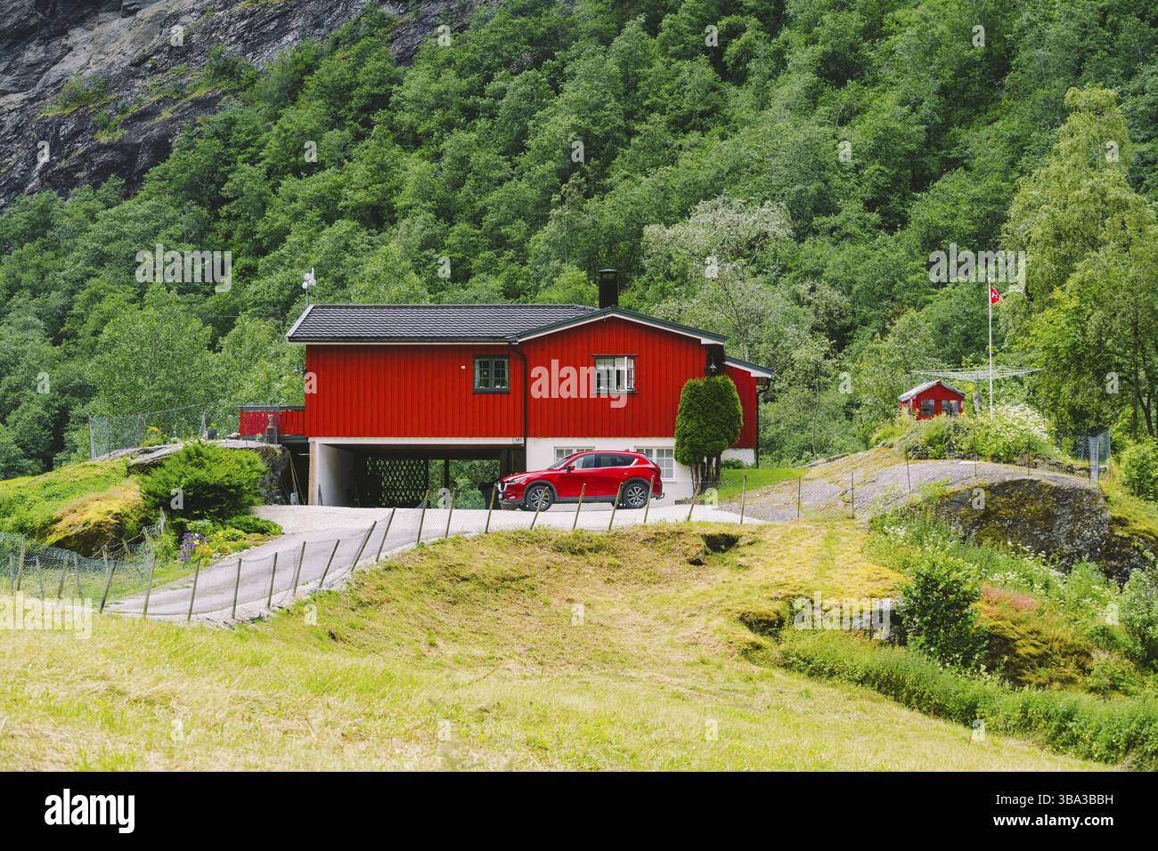 Casa rossa in legno e auto nella città norvegese Flam. Casa di campagna e auto in giardino. Cottage in montagna Foto Stock