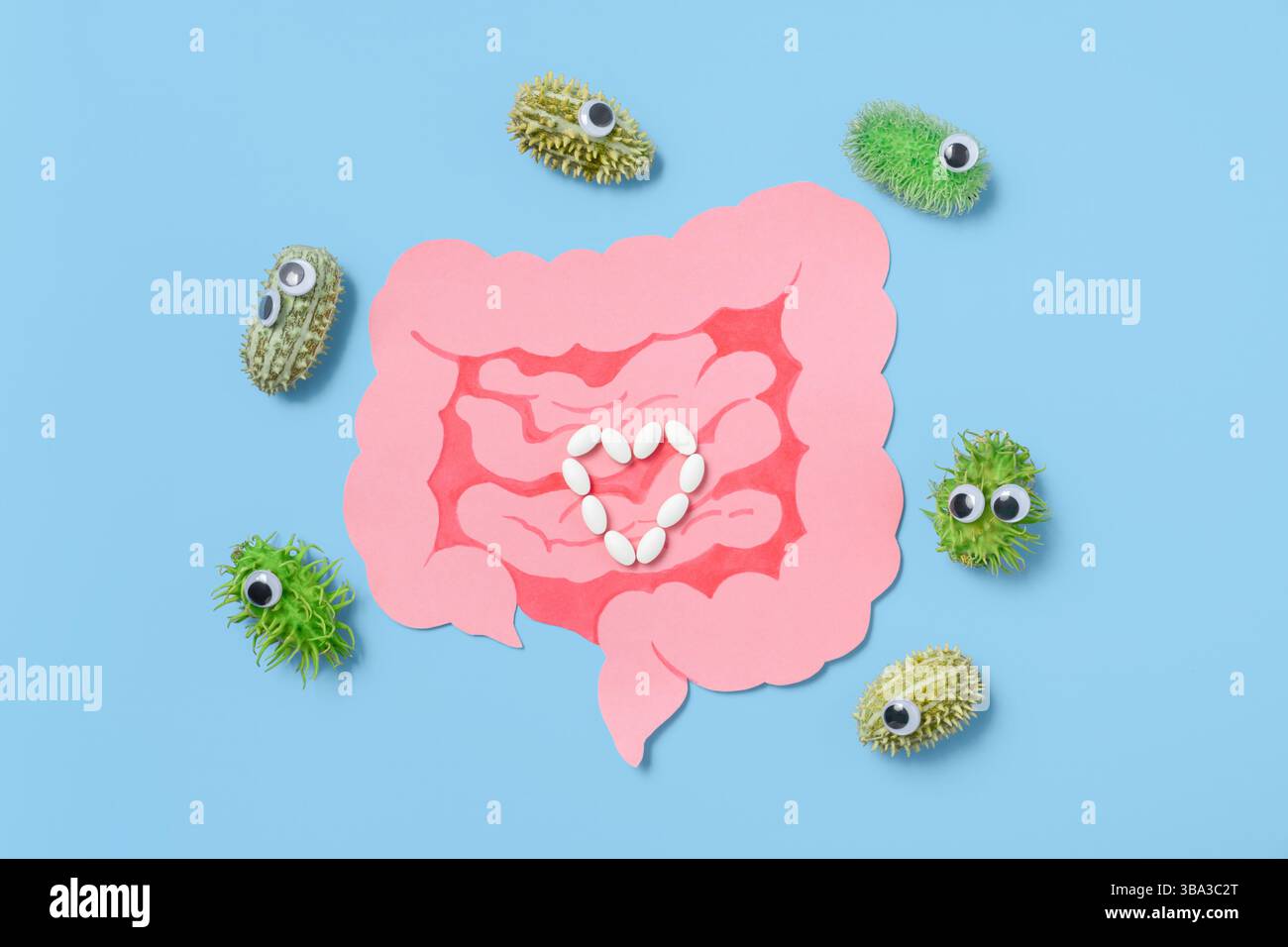 Pillole bianche disposte in un cuore all'interno di intestini rosa con batteri cartoni animati con occhi strani su sfondo blu. Salute digestiva, probiotici Foto Stock