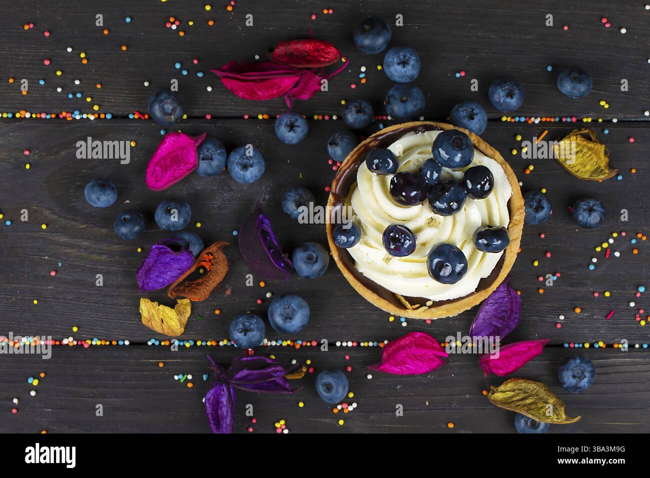 Su una tavola di legno giace una torta con panna e mirtilli Foto Stock