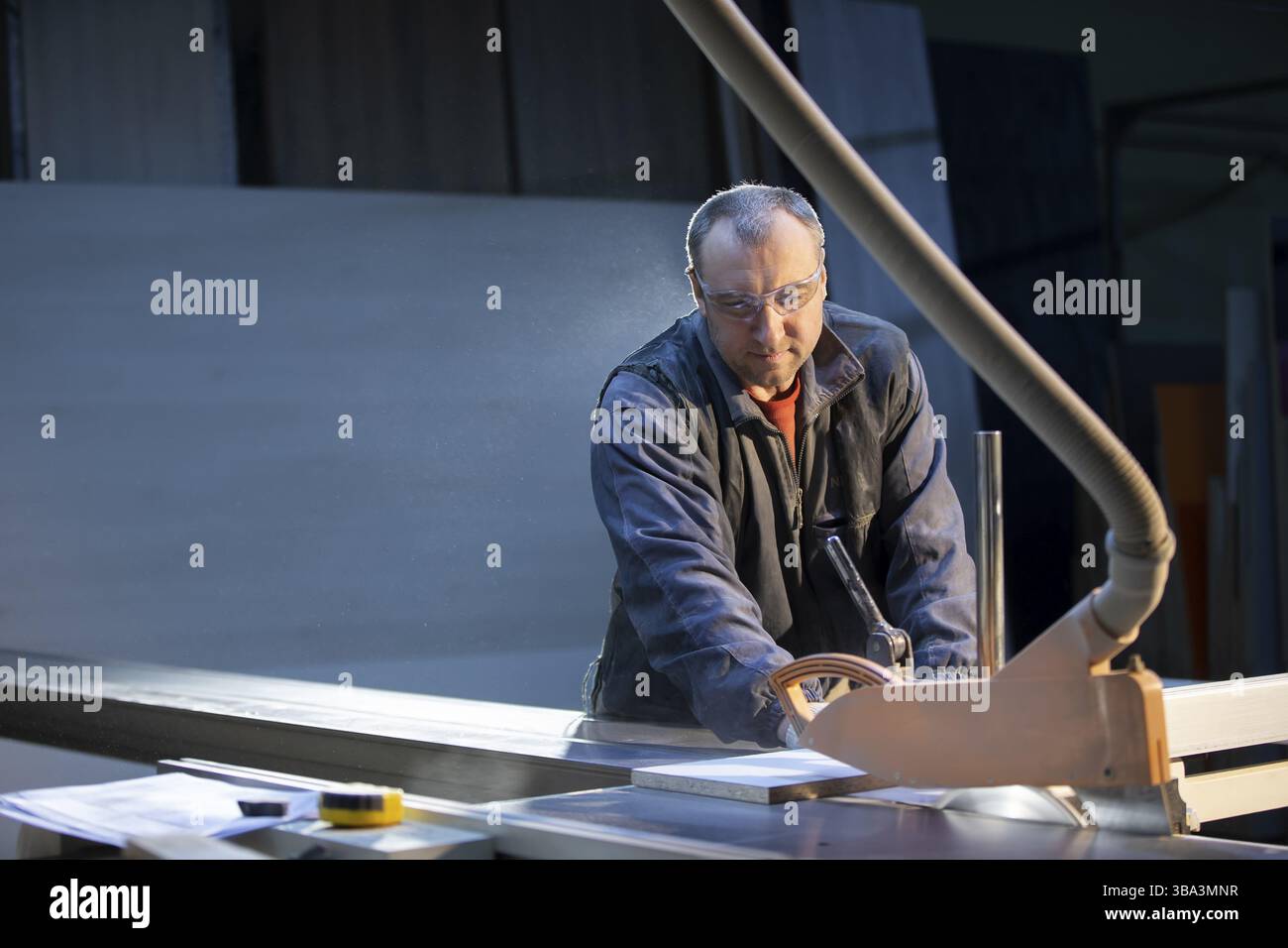 Un lavoratore di produzione di mobili in una macchina di taglio produce parti di mobili. Produzione di mobili Foto Stock