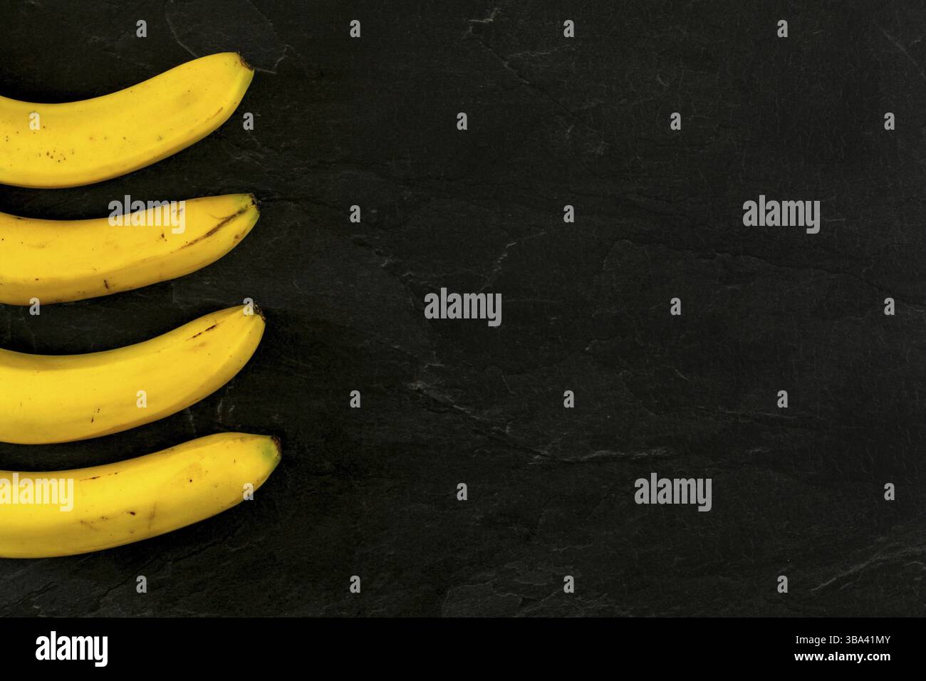 Quattro banane su ardesia nera come foto da tavola dall'alto, solo una parte visibile, più spazio per il testo lato destro, Liptovsky Hradok, Slovacchia, Europa Foto Stock