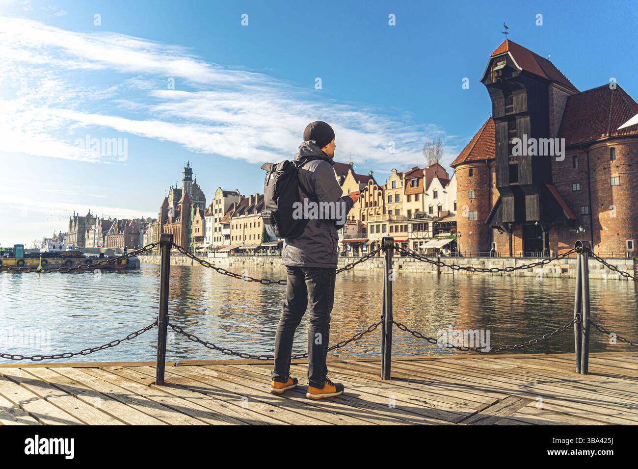 Tema del turismo in Polonia. Viaggio a Danzica. Un viaggiatore maschile utilizza un telefono sull'argine del fiume Motlawa in mezzo all'attrazione principale, un simbo Foto Stock