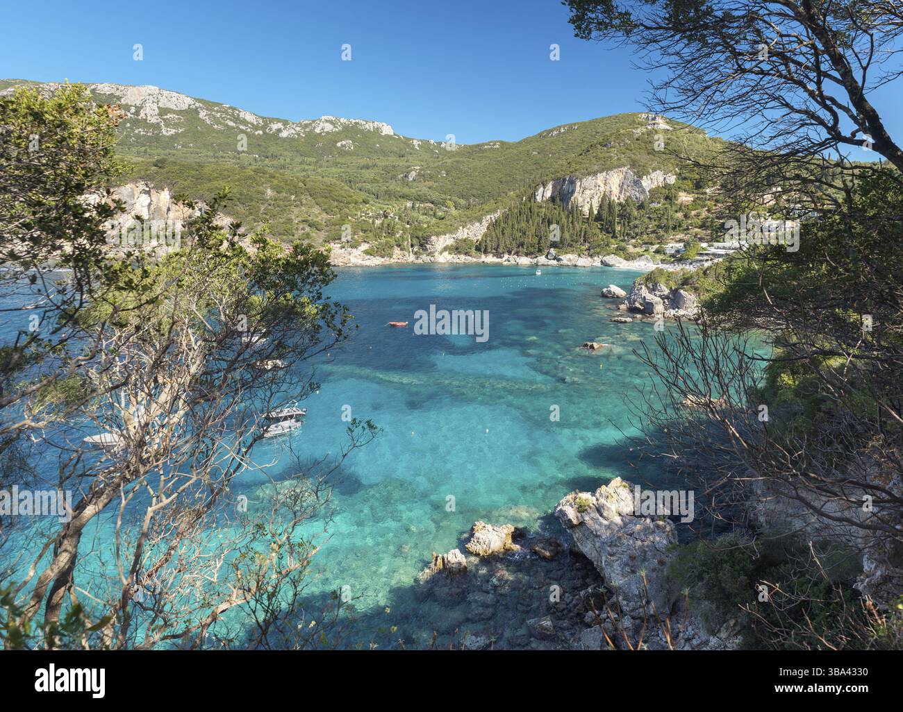 Sonne scheint blaues Meer an der Bucht von Liapades zu beruhigen, Blick von der kleinen felsigen Klippe in der naehe, gruene Nadelbaeume und Buesche i Foto Stock