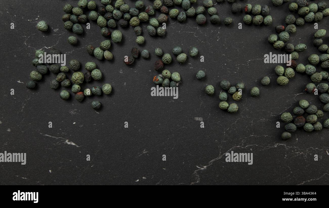 Vista dall'alto verso il basso, pepe nero (Piper nigrum) versato su una tavola di lavoro scura. Variante verde turco / mais piccante blu, Liptovsky Hradok, Slovacchia, E. Foto Stock