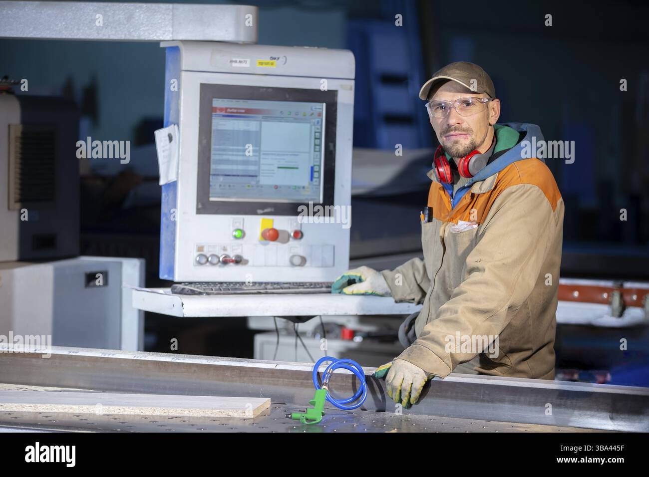 Un lavoratore di produzione di mobili dietro una macchina programmata produce parti di mobili. Produzione di mobili Foto Stock
