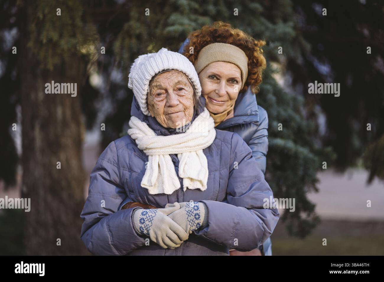 Donne caucasiche madre anziana e figlia matura in giardino d'inverno sullo sfondo abete albero abbracciarsi faccia a faccia, sorridere, trascorrere il tempo con la vecchia lepre Foto Stock