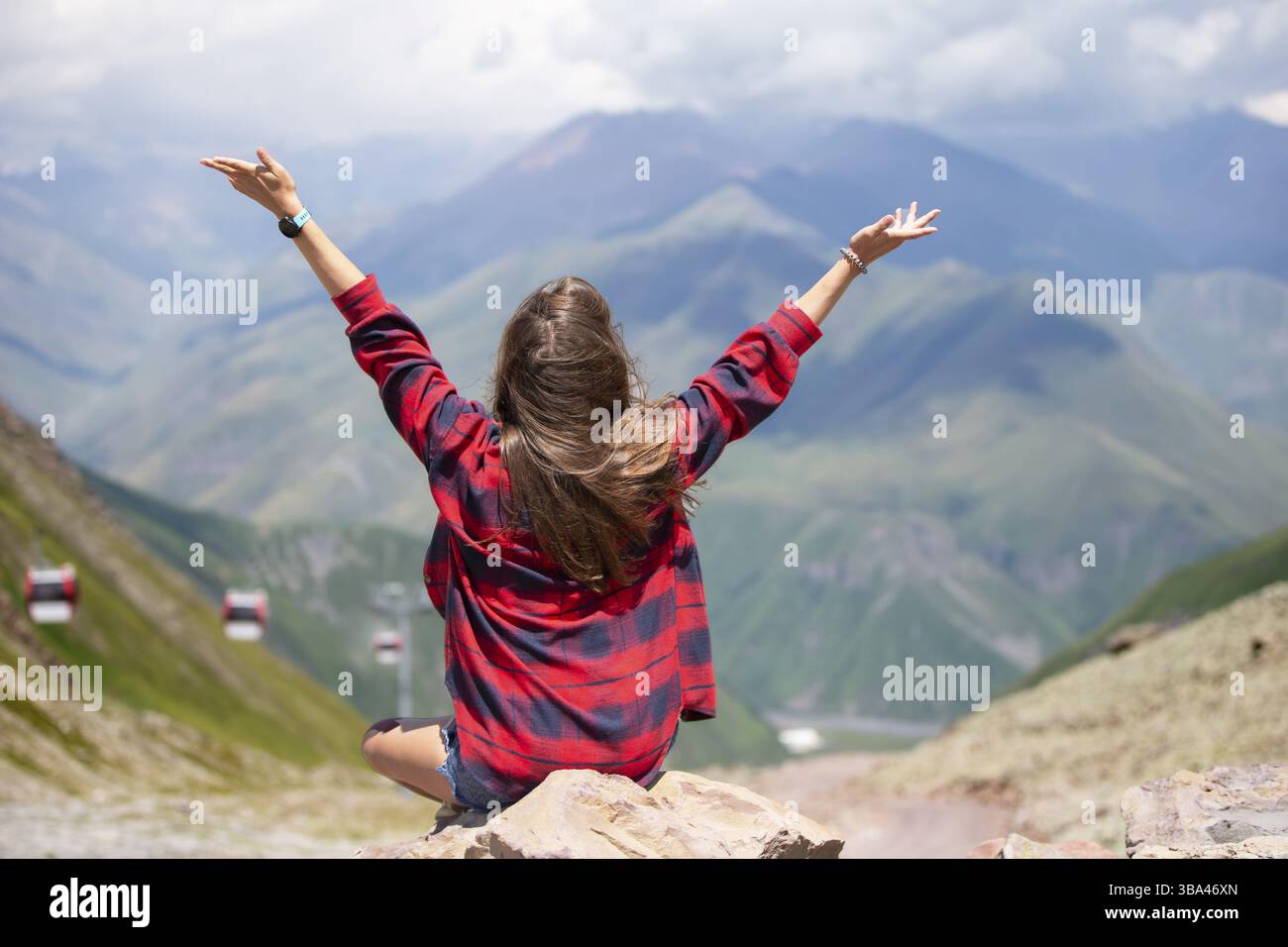 Donna felice turistica sulla cima della montagna ha alzato le mani in alto, gode di una splendida vista sulle montagne Foto Stock