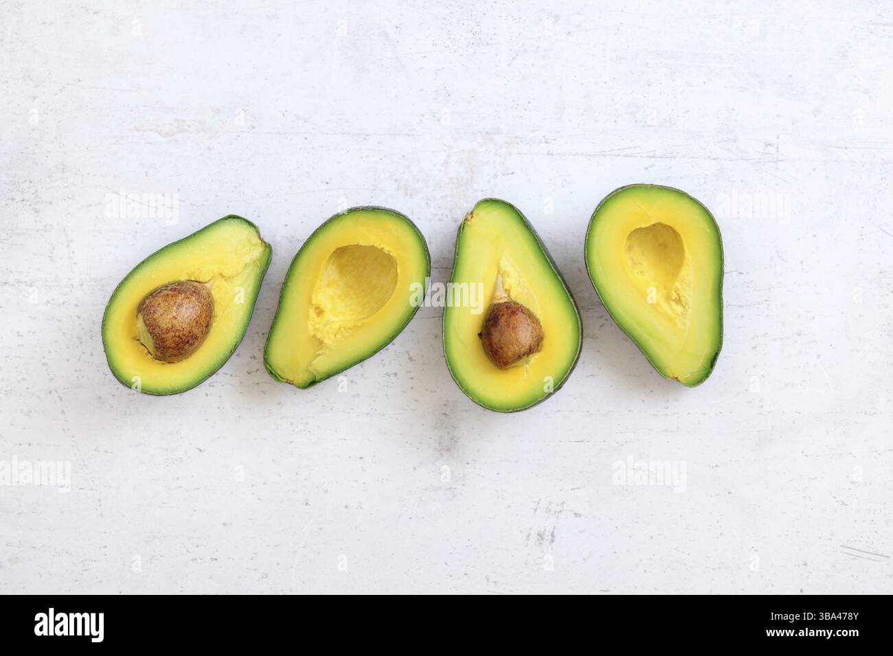 Vista dall'alto verso il basso, due avocado tagliati a metà, metà con semi visibili, su una tavola di pietra bianca. Spazio per il testo sopra e sotto, Liptovsky Hradok, Slova Foto Stock