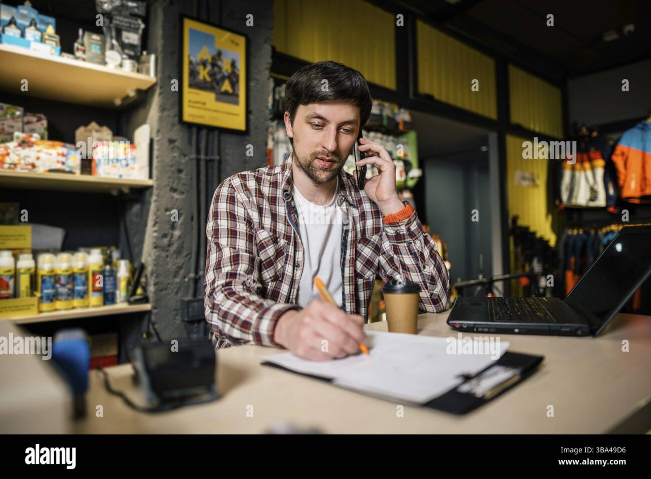Titolare di una piccola azienda al telefono e al computer in negozio. Operaio di negozio di sport che effettua la chiamata con il telefono delle cellule. Venditore che lavora e parla sul telefono delle cellule in bicy Foto Stock