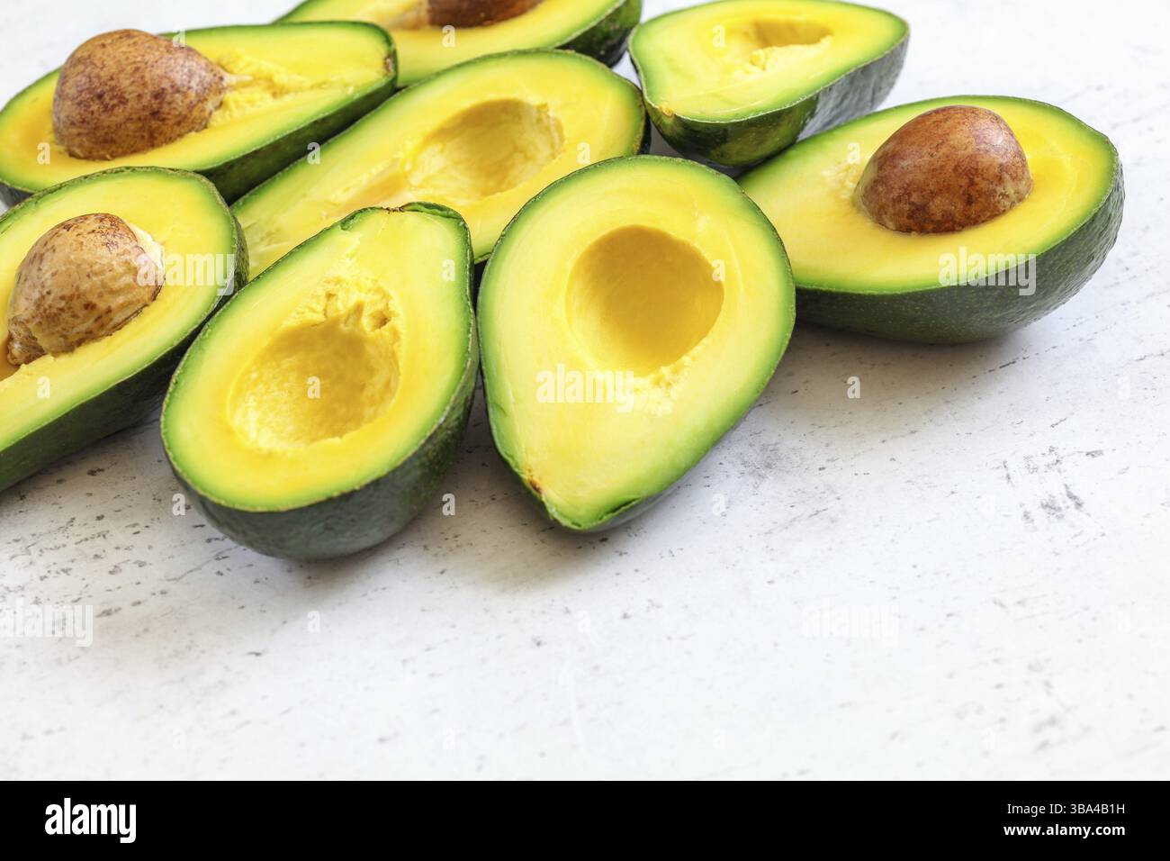 Metà avocado con polpa verde gialla, alcuni semi marroni visibili sulla lavagna di lavoro bianca - spazio per testo Right Down, Liptovsky Hradok, Slovacchia, Europa Foto Stock