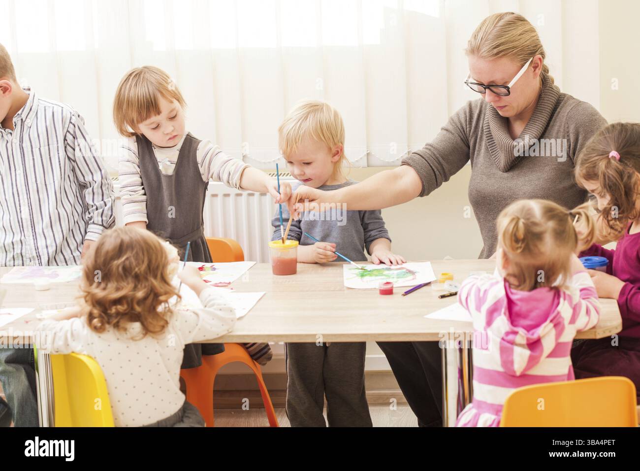 I bambini e i tutor sono la verniciatura con un pennello e acquerelli su carta nella scuola materna Foto Stock