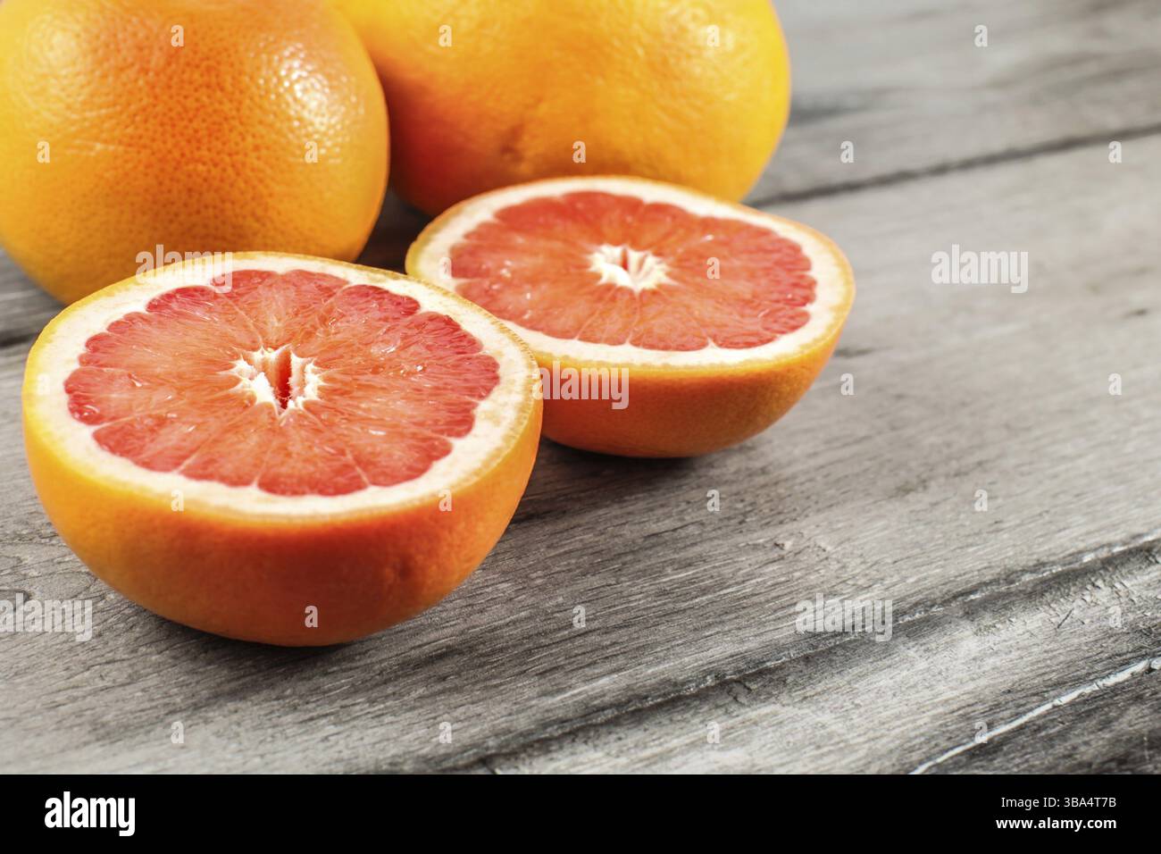 Pompelmo rosso rosa tagliato a metà, con due interi sullo sfondo su tavola di legno grigio, Liptovsky Hradok, Slovacchia, Europa Foto Stock