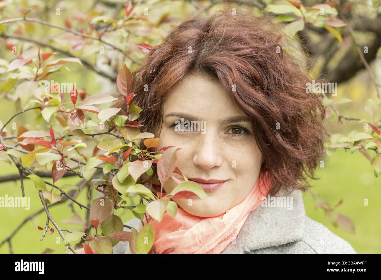 Bella donna romantica con i rami di mele foglie rosse nel parco primaverile. Sfondo degli alberi primaverili. Primo piano verticale Foto Stock