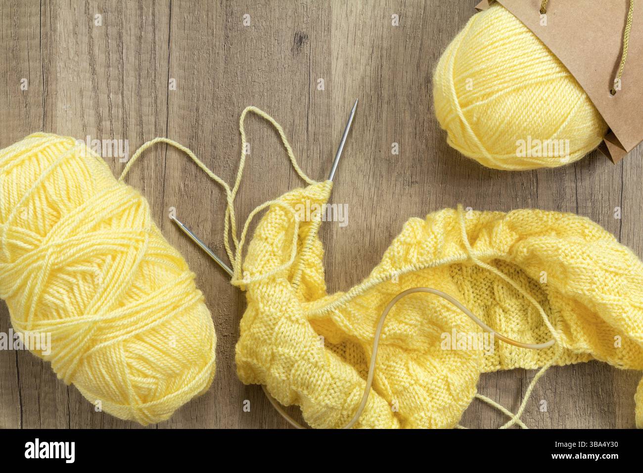 Lana per maglieria giallo chiaro e aghi per maglieria su fondo in legno. Vista superiore.spazio copia. Tessuti e filati lavorati a maglia su una superficie in legno Foto Stock