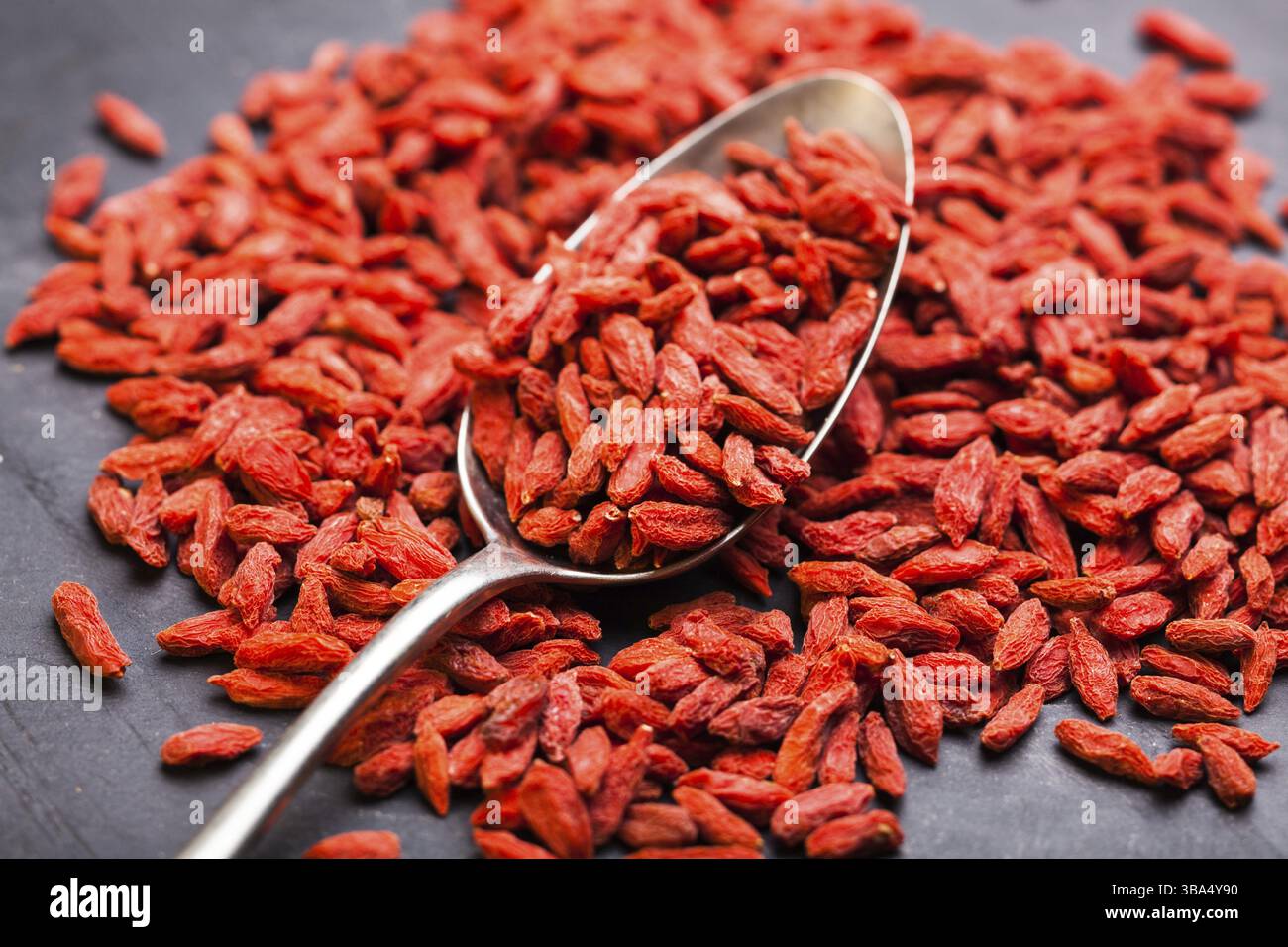 Cucchiaio di acciaio di bacche di goji rosse su fondo scuro Foto Stock